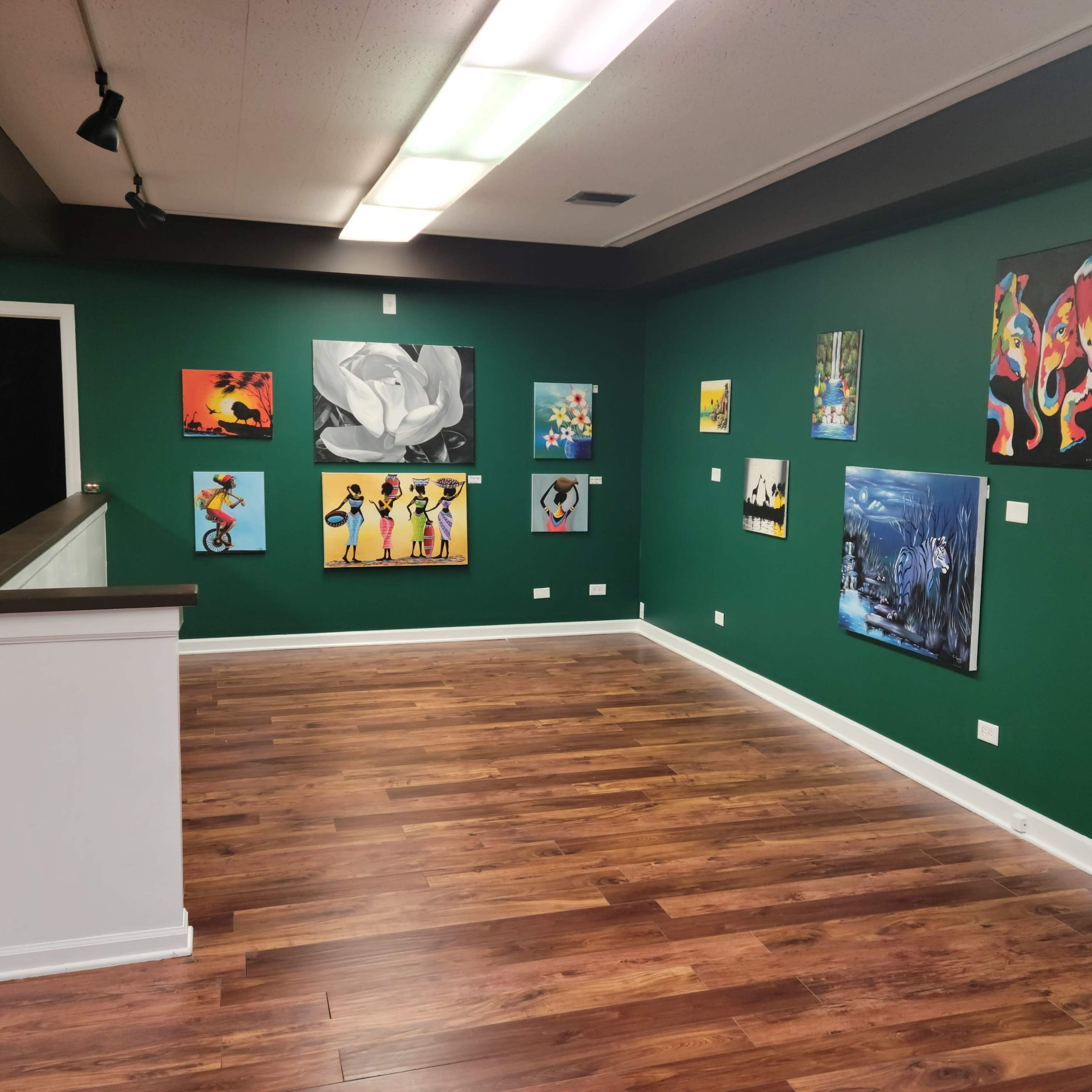 A gallery interior with green walls displaying various colorful paintings and a wooden floor.