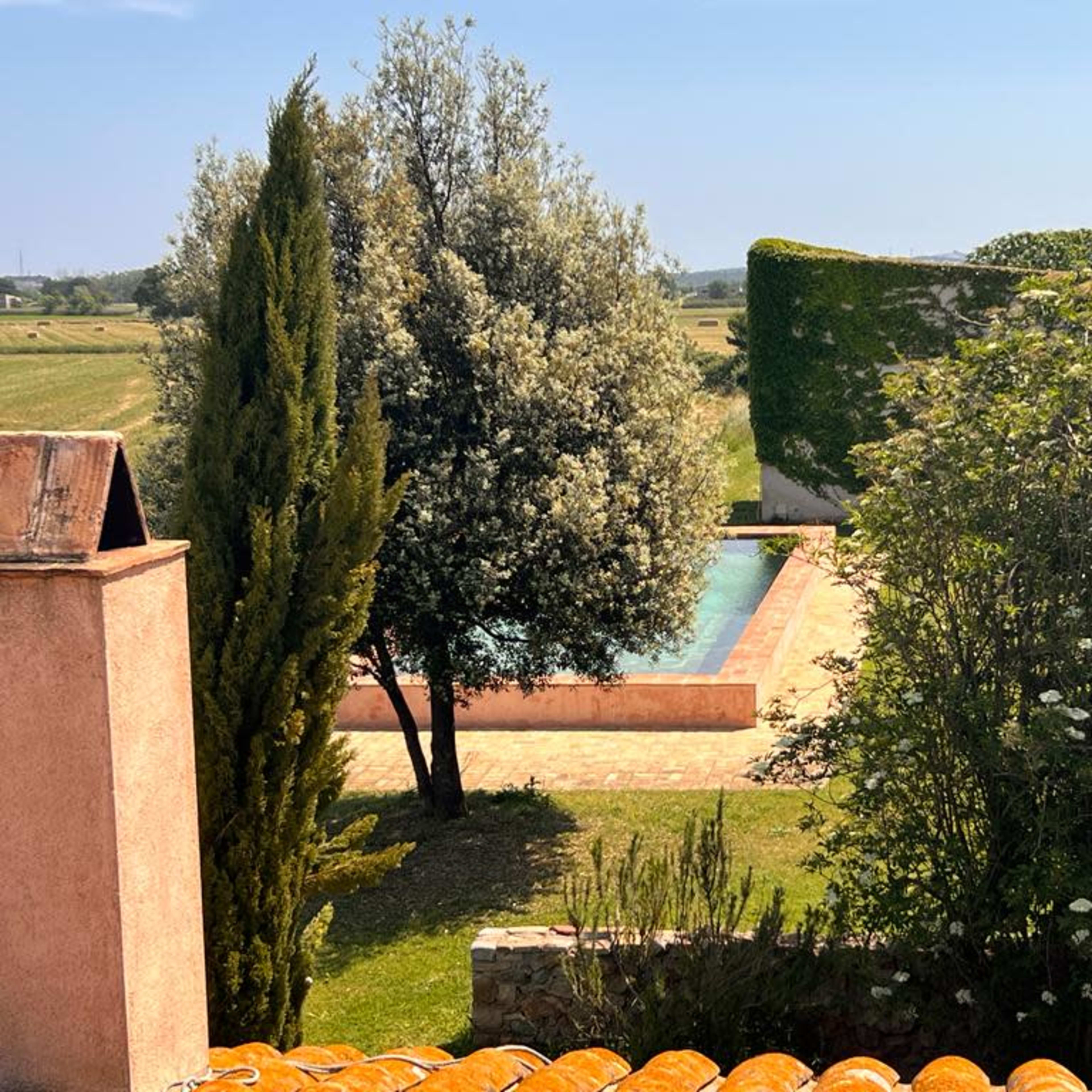 A landscaped outdoor area featuring a swimming pool surrounded by greenery and a terracotta roof.