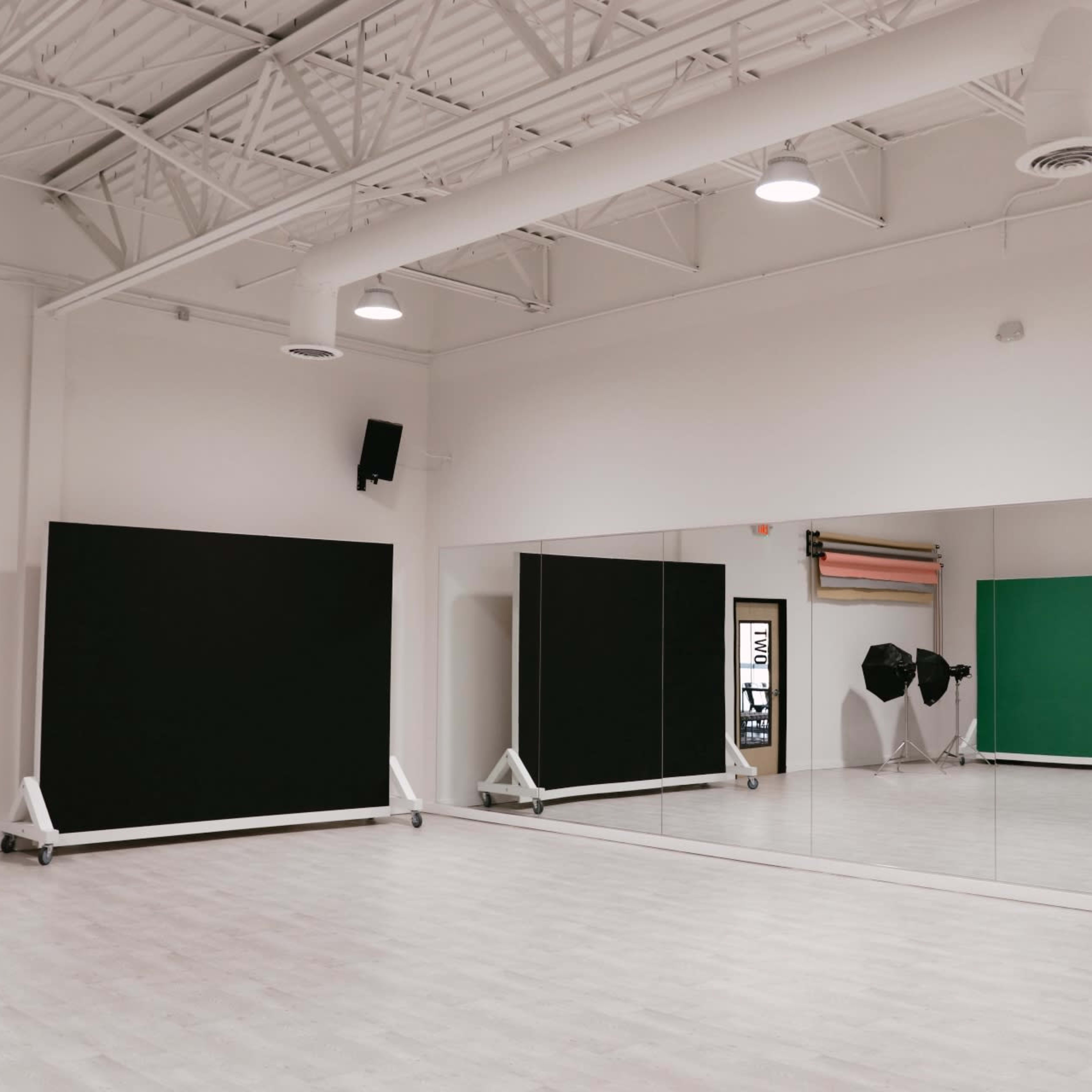 A spacious photography studio with large mirrors, green and black backdrops, and softbox lighting setups.