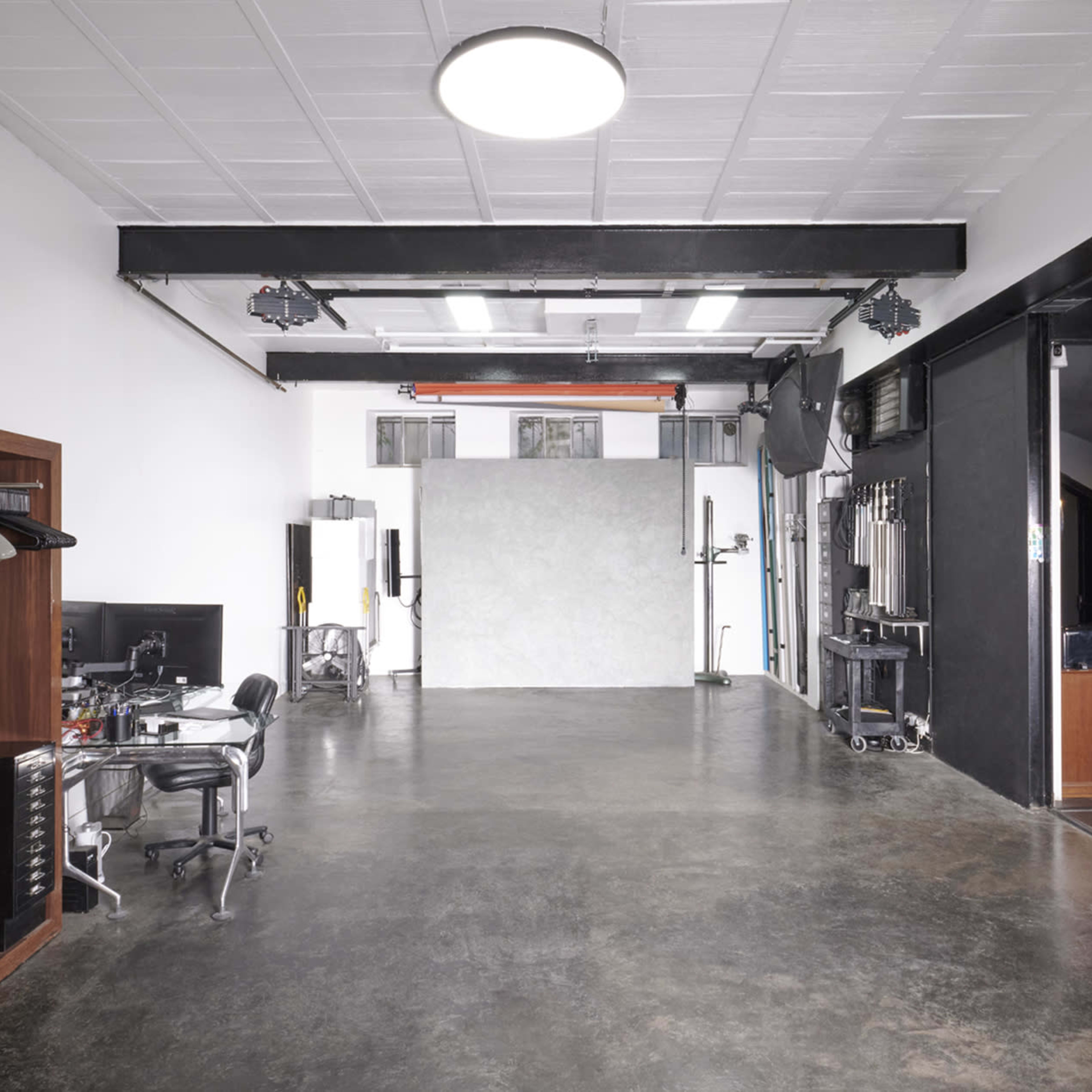 A spacious, well-lit studio with a gray backdrop, a black office chair, and a clothing rack against one wall.