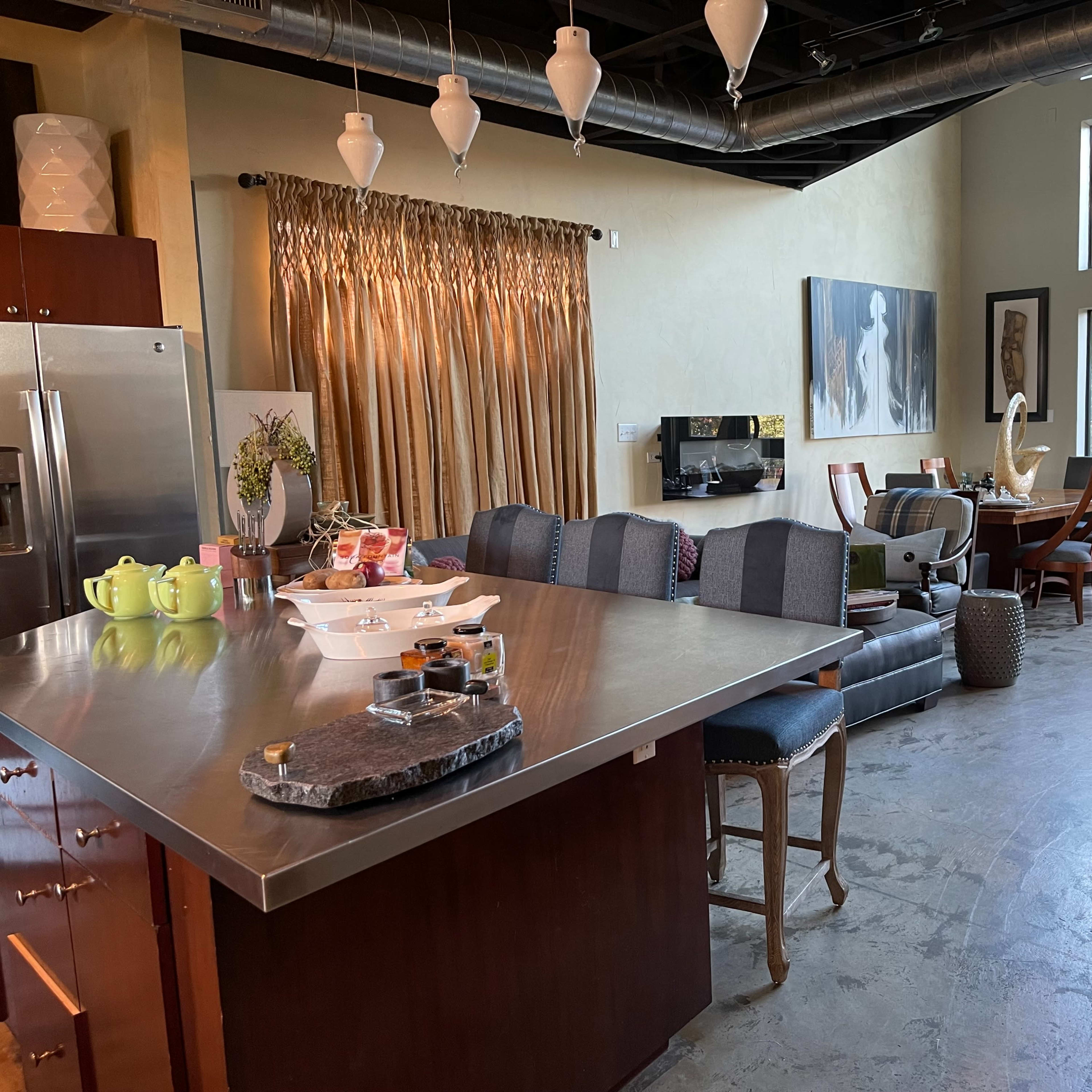 A modern kitchen and living area with a large island, dining table, and windows letting in natural light.