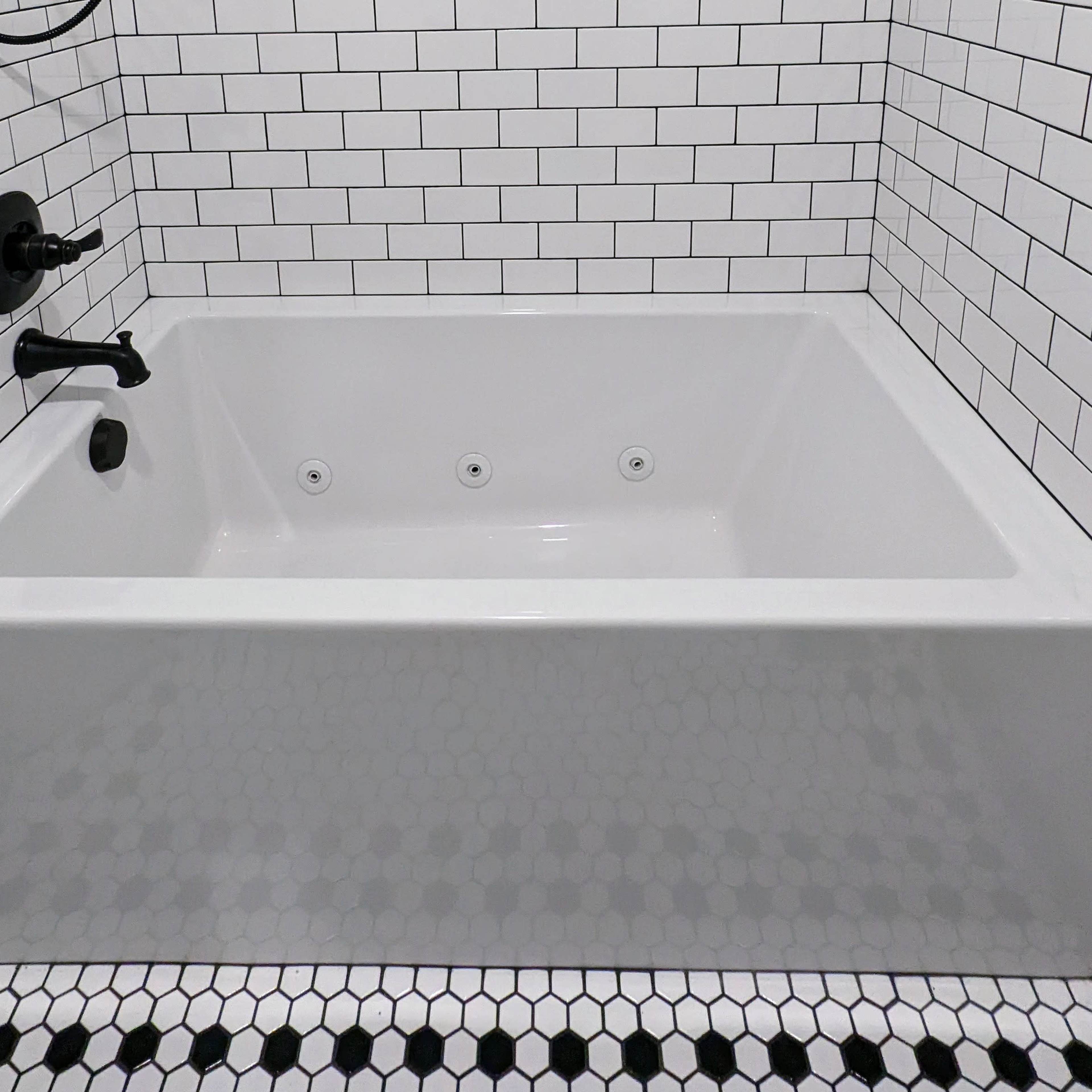A corner bathtub surrounded by black and white tiled walls and flooring.