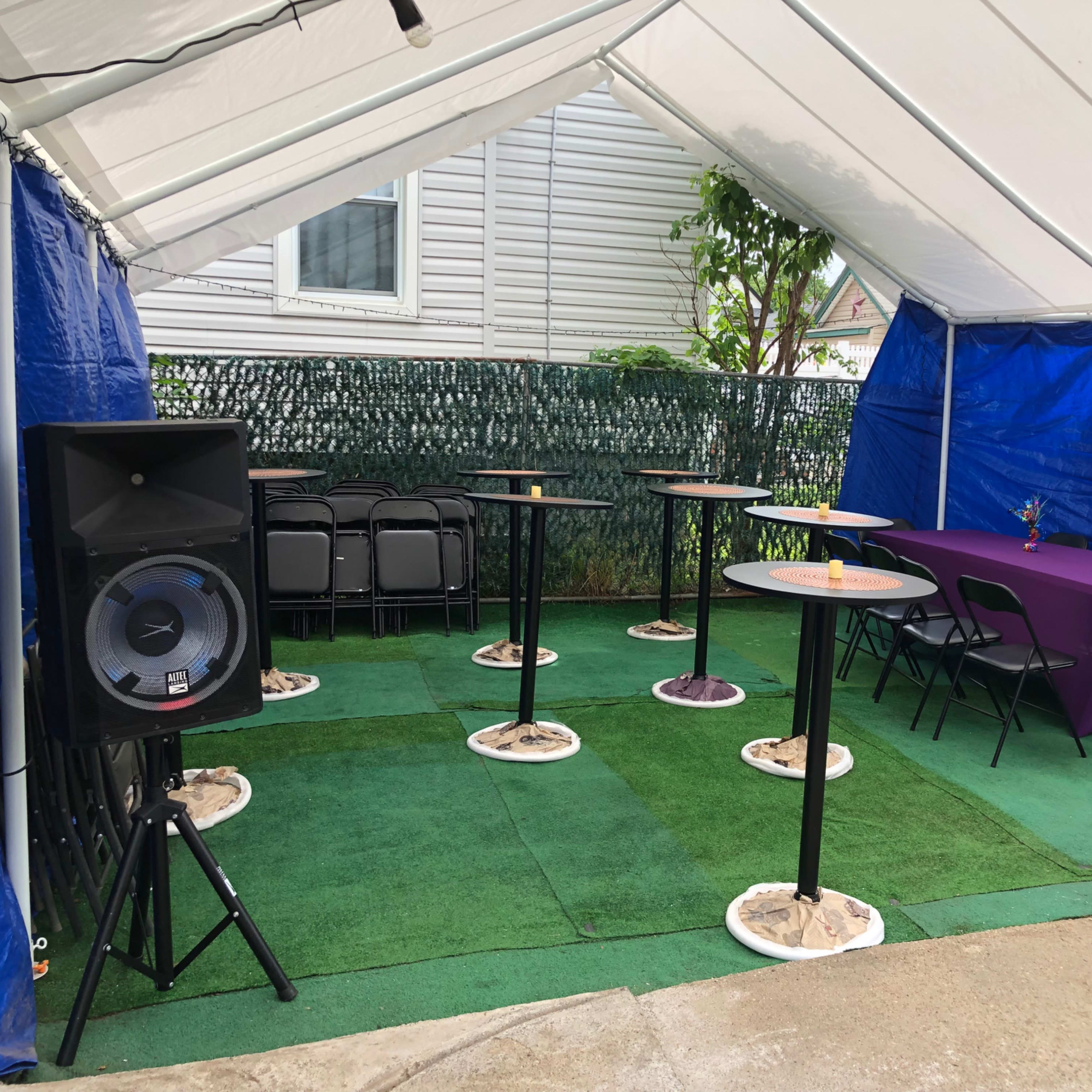 A tented area with several standing tables, chairs, and a purple tablecloth set up for a gathering.