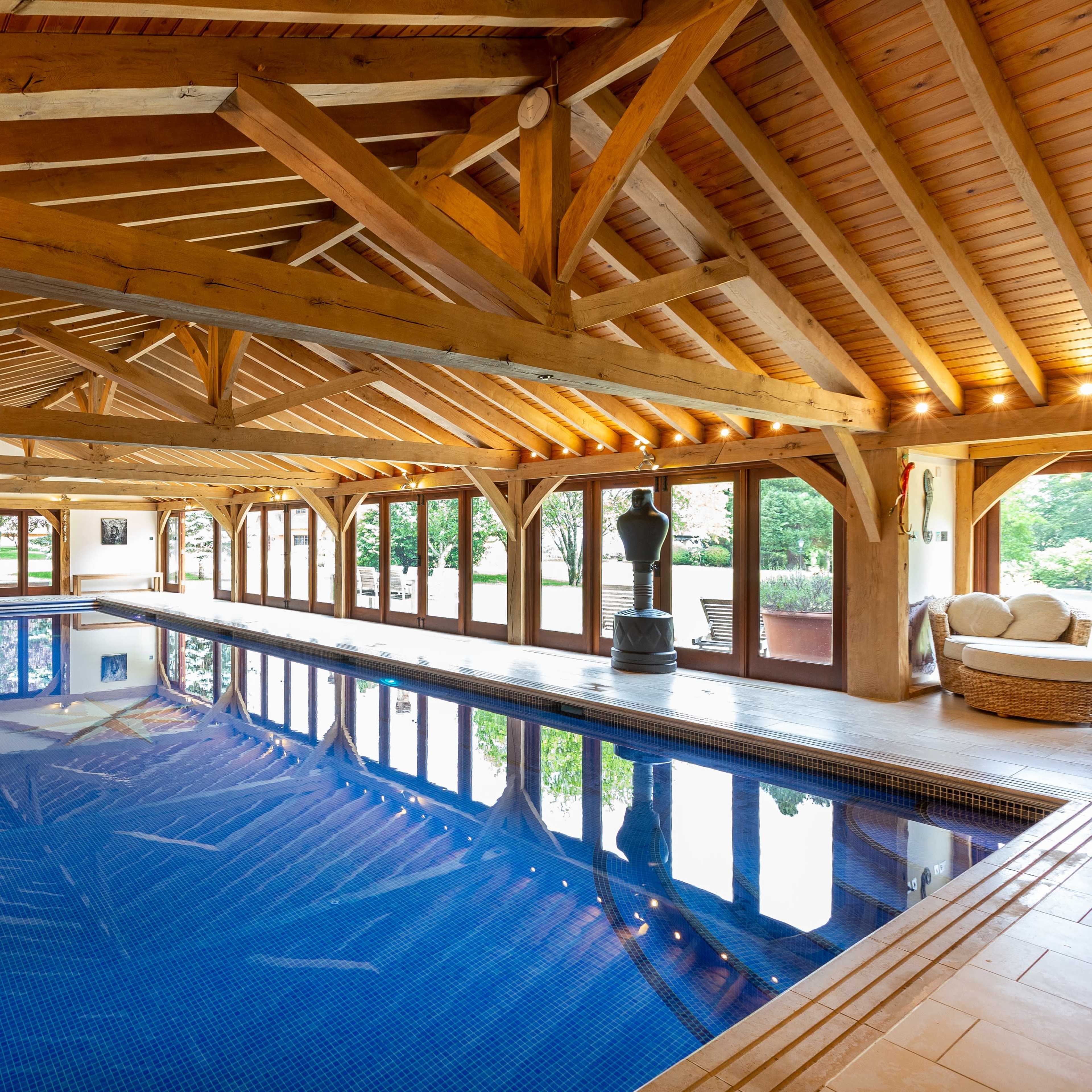 An indoor swimming pool with a wooden roof, large windows, and a serene ambiance.