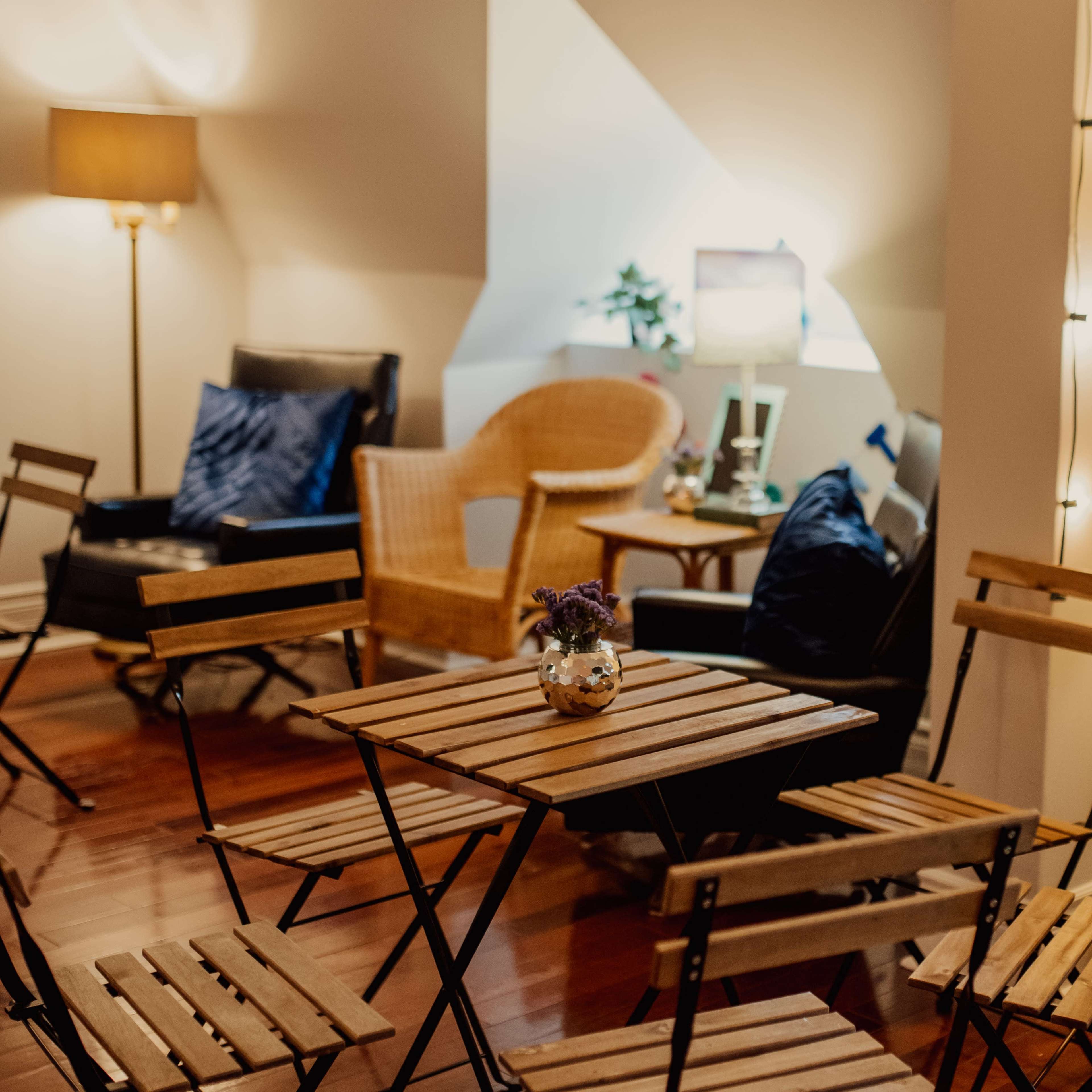 The scene features a cozy room with wooden folding chairs and a small table at the center, surrounded by soft lighting and seating areas.