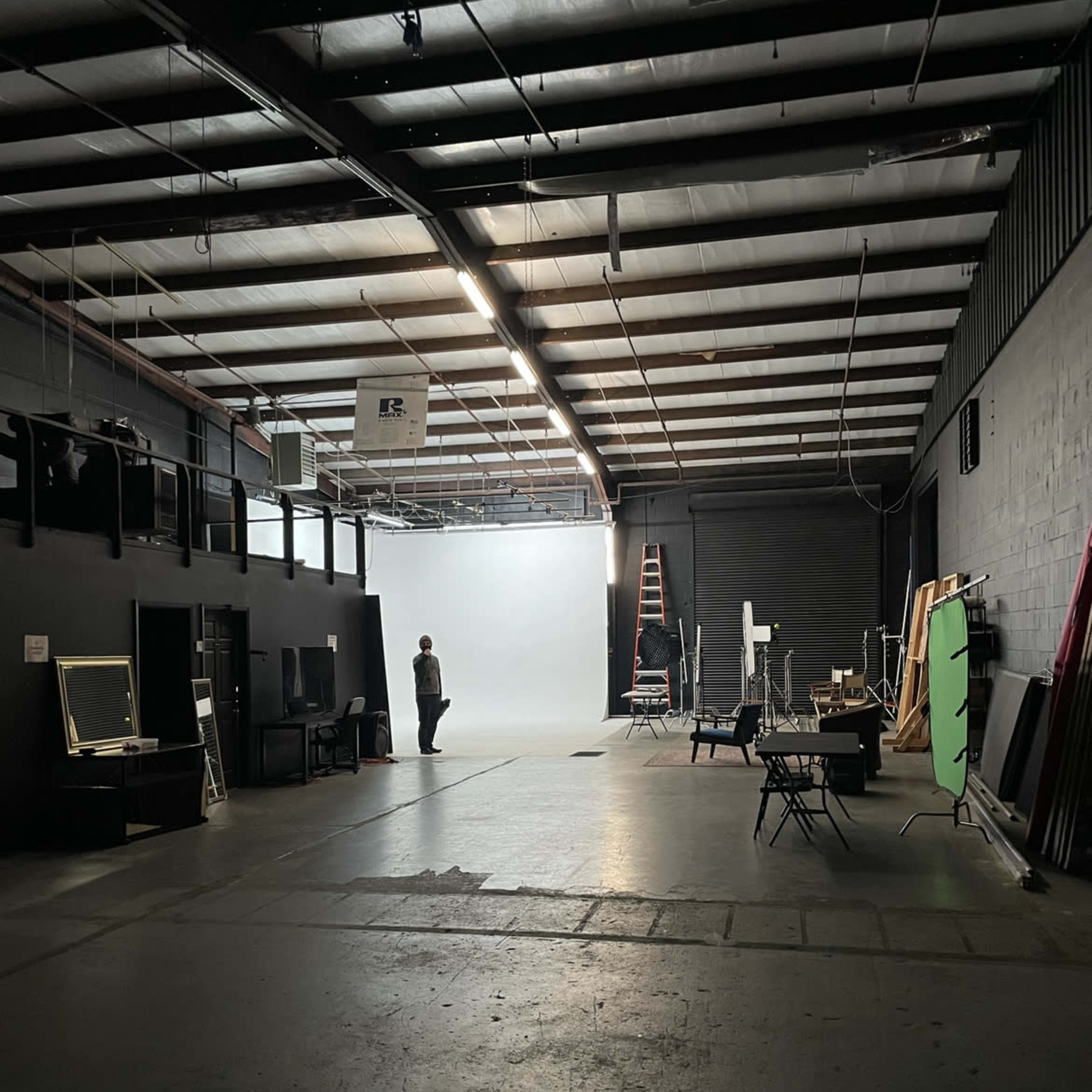 A person stands in a spacious studio with a light gray backdrop, surrounded by various equipment and props.