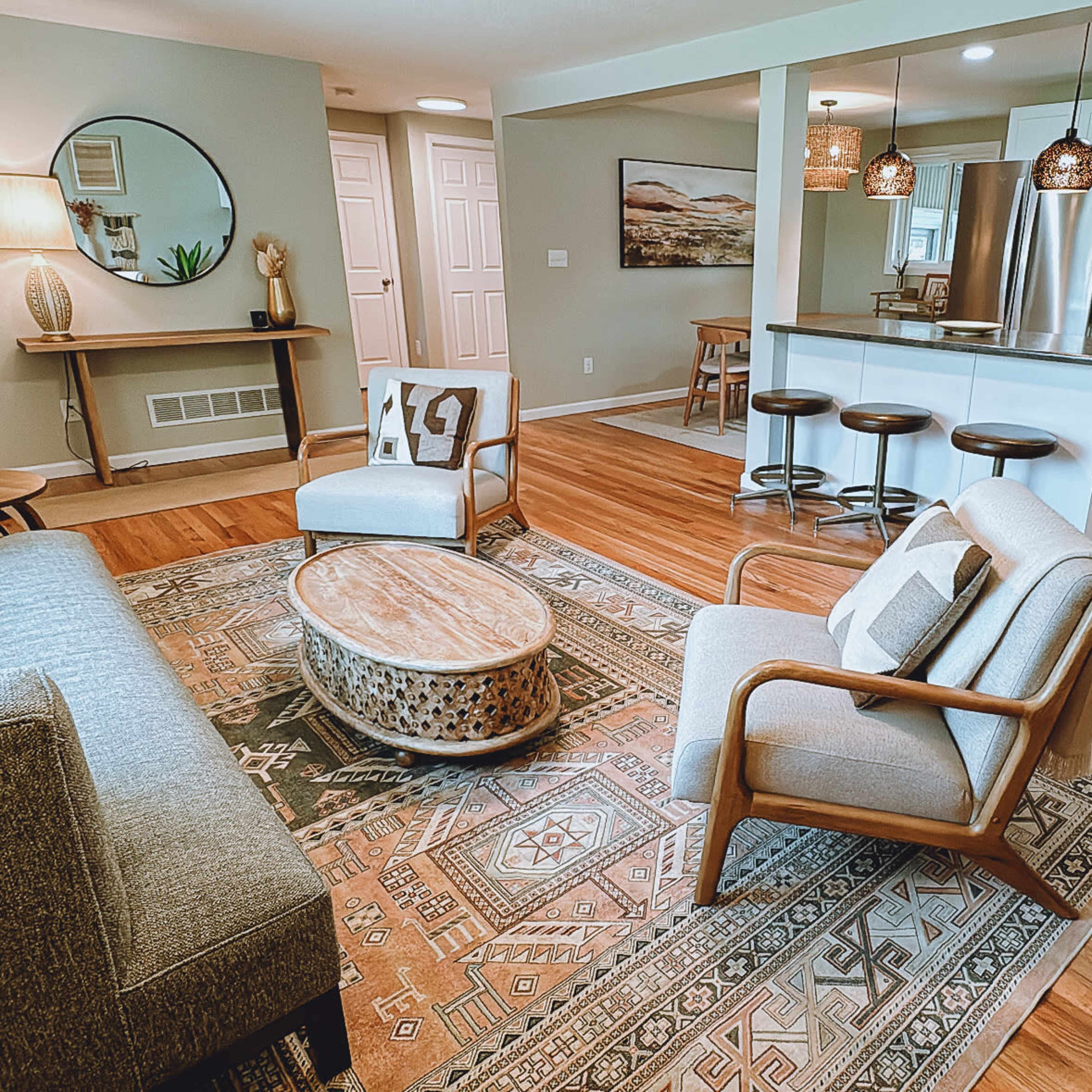 A modern living room with a sofa, armchairs, a coffee table, and an open kitchen area in a home featuring hardwood floors and neutral-colored walls.