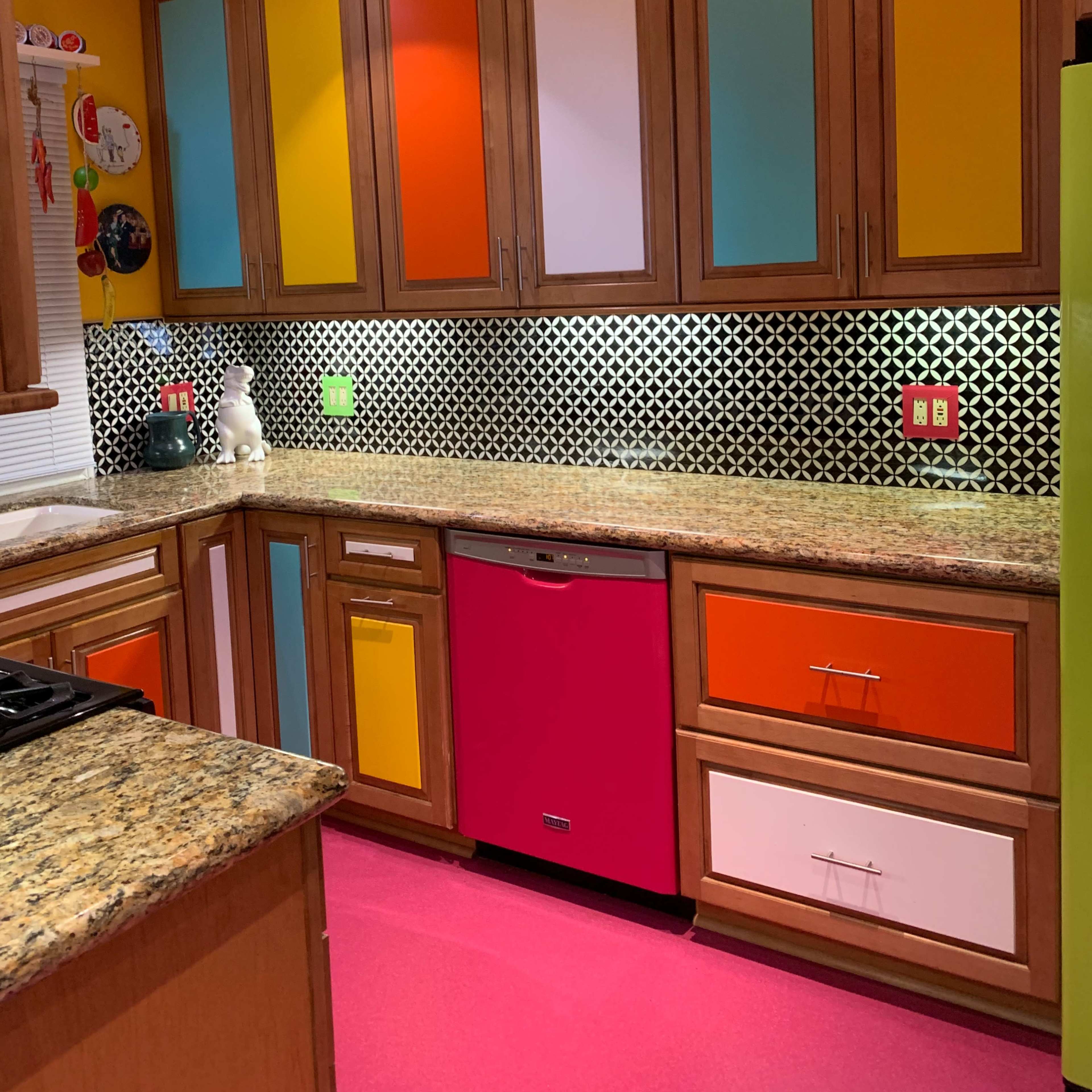 The kitchen features wooden cabinets with colorful panels, a pink dishwasher, and a black and white patterned backsplash.