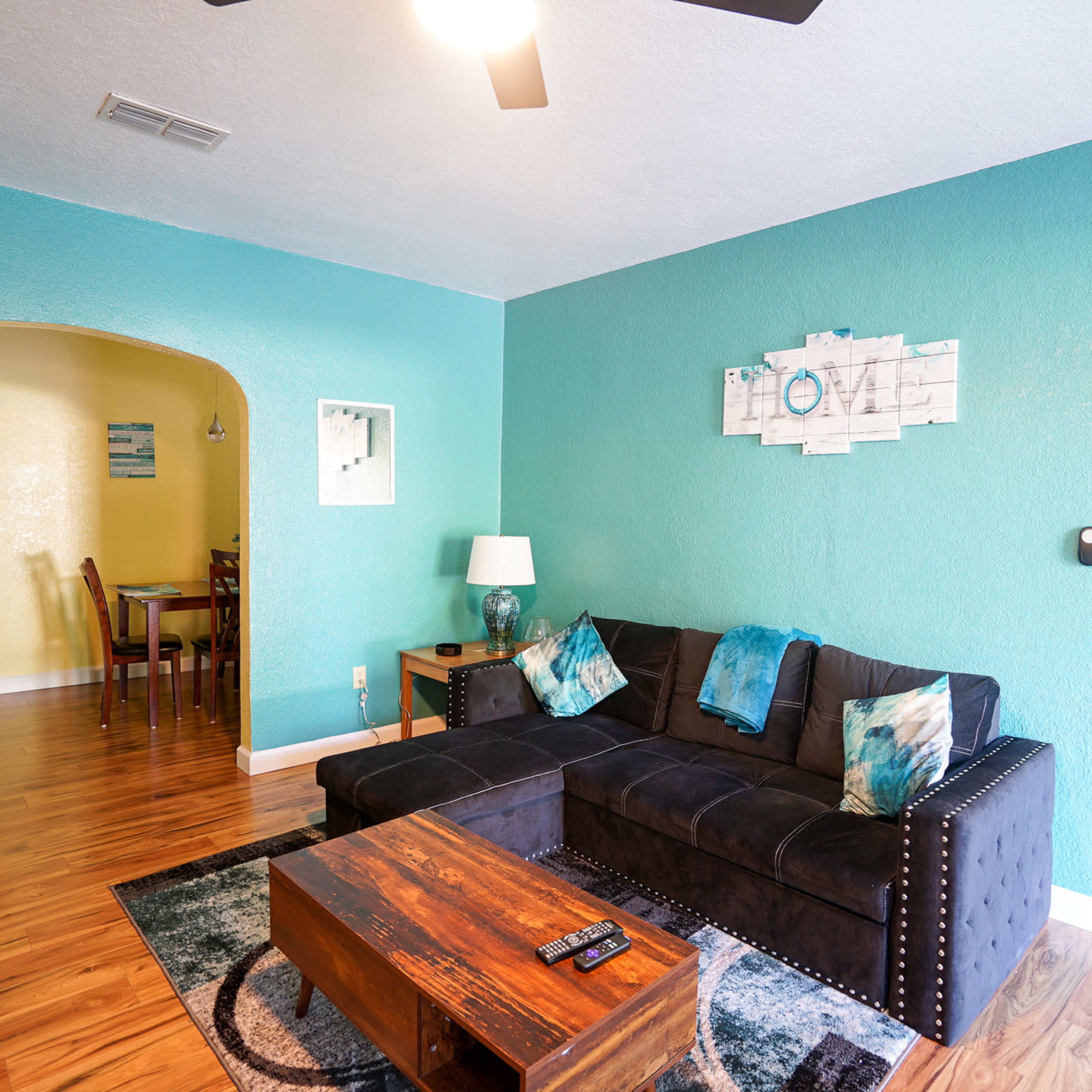 The living room features a dark sectional sofa and a wooden coffee table, with turquoise walls and hardwood flooring.