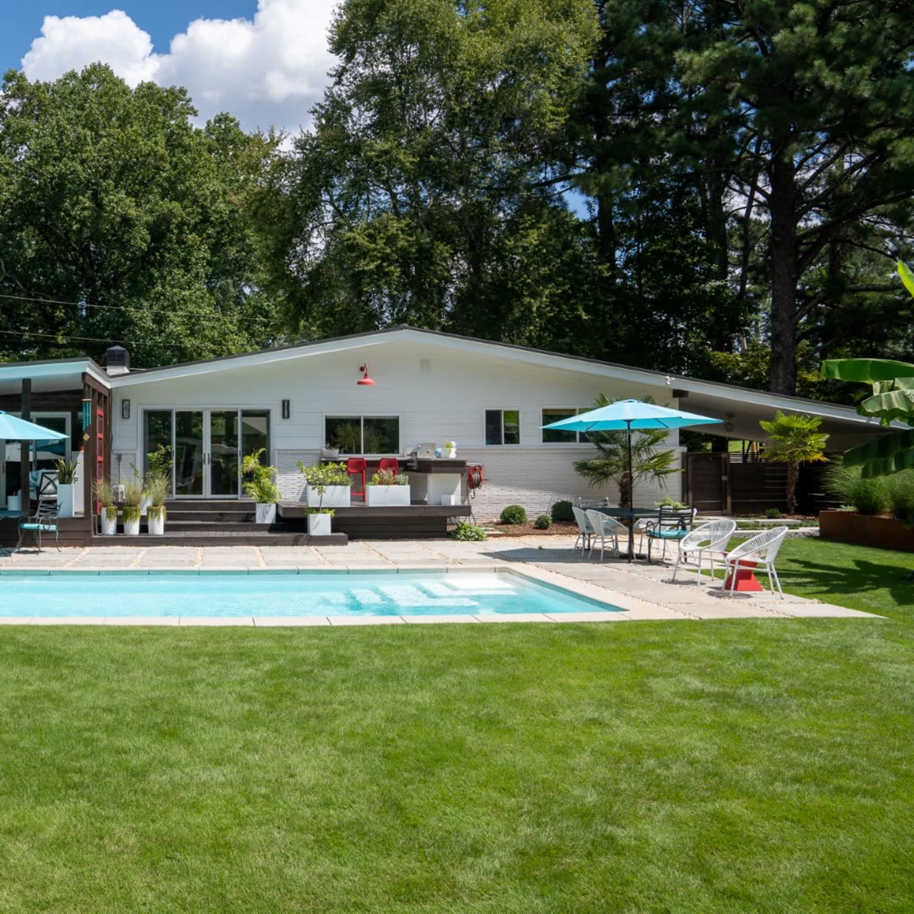 A modern house with a swimming pool and patio is surrounded by a green lawn and trees.