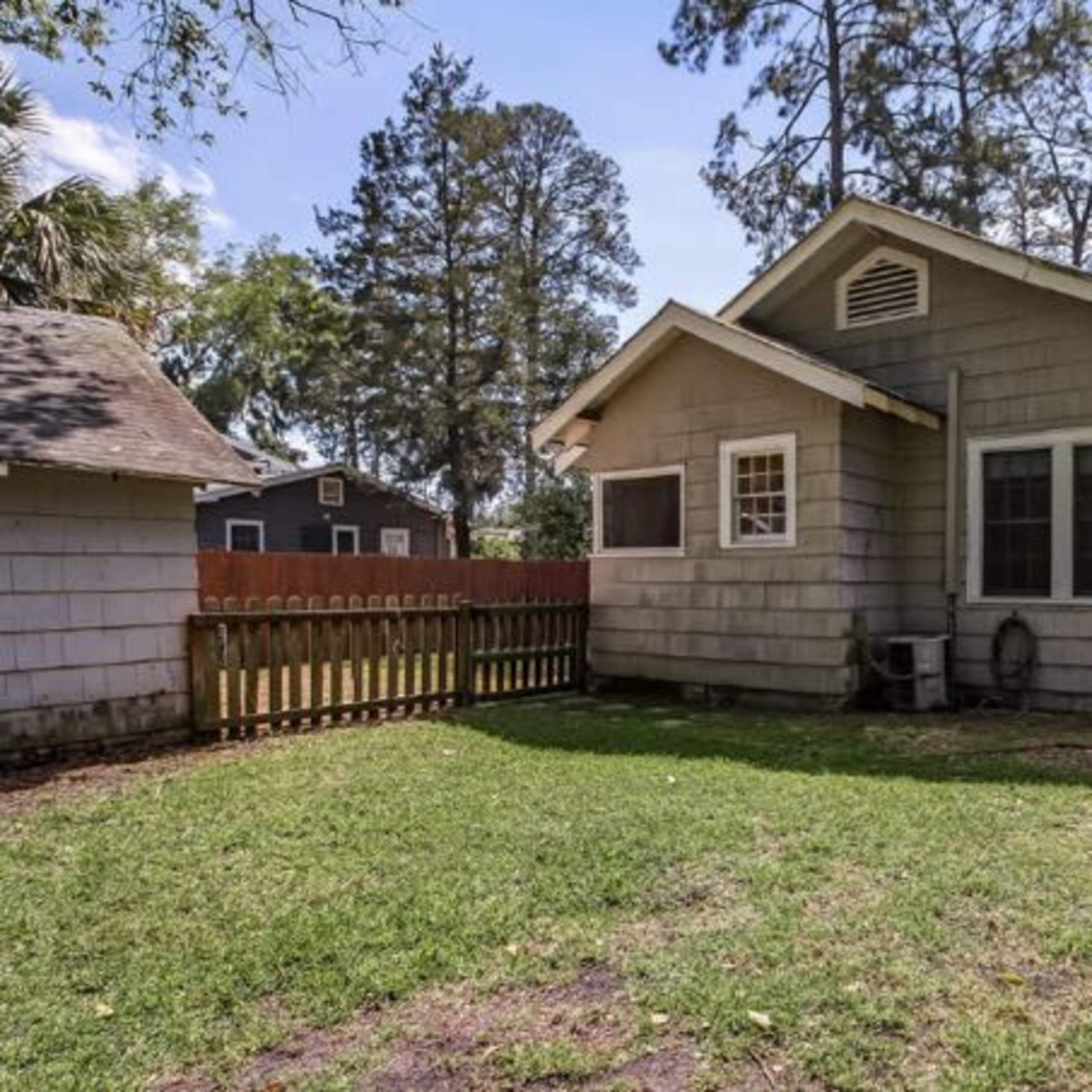 The backyard of a house with a grassy area, wooden fence, and trees in the background.