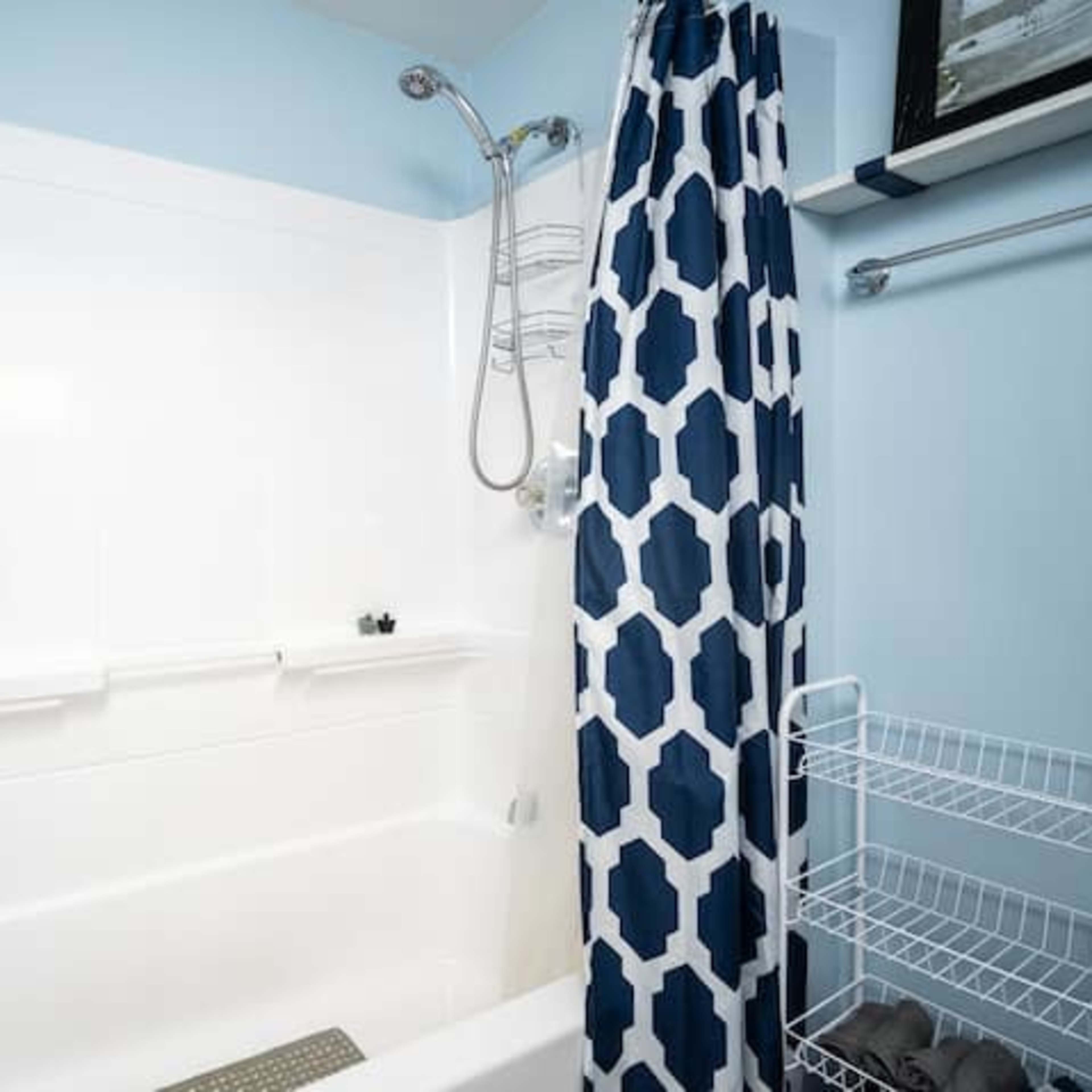 A clean bathroom features a white bathtub with a blue wall and patterned shower curtain.
