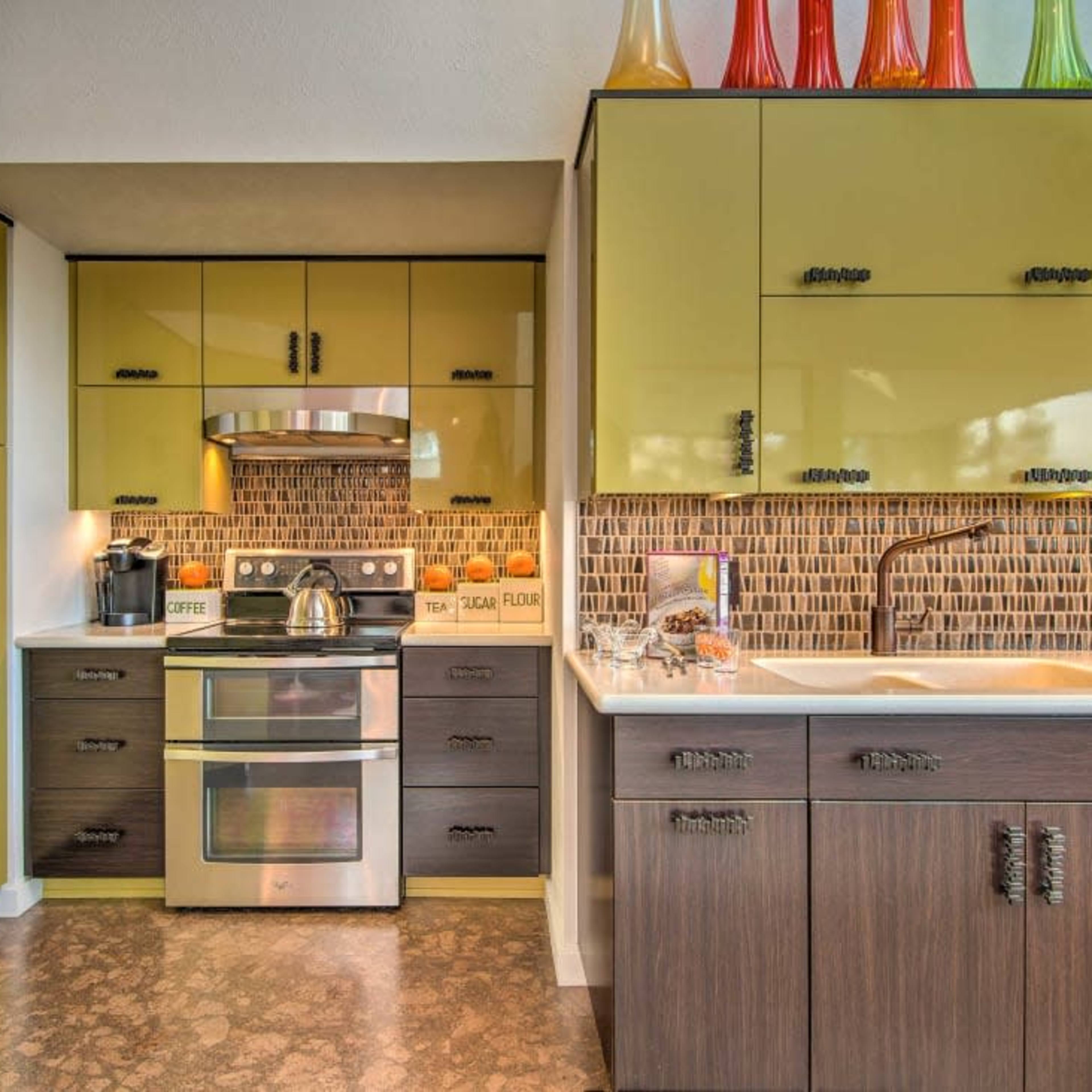 A modern kitchen with green cabinetry, stainless steel appliances, and a patterned backsplash.