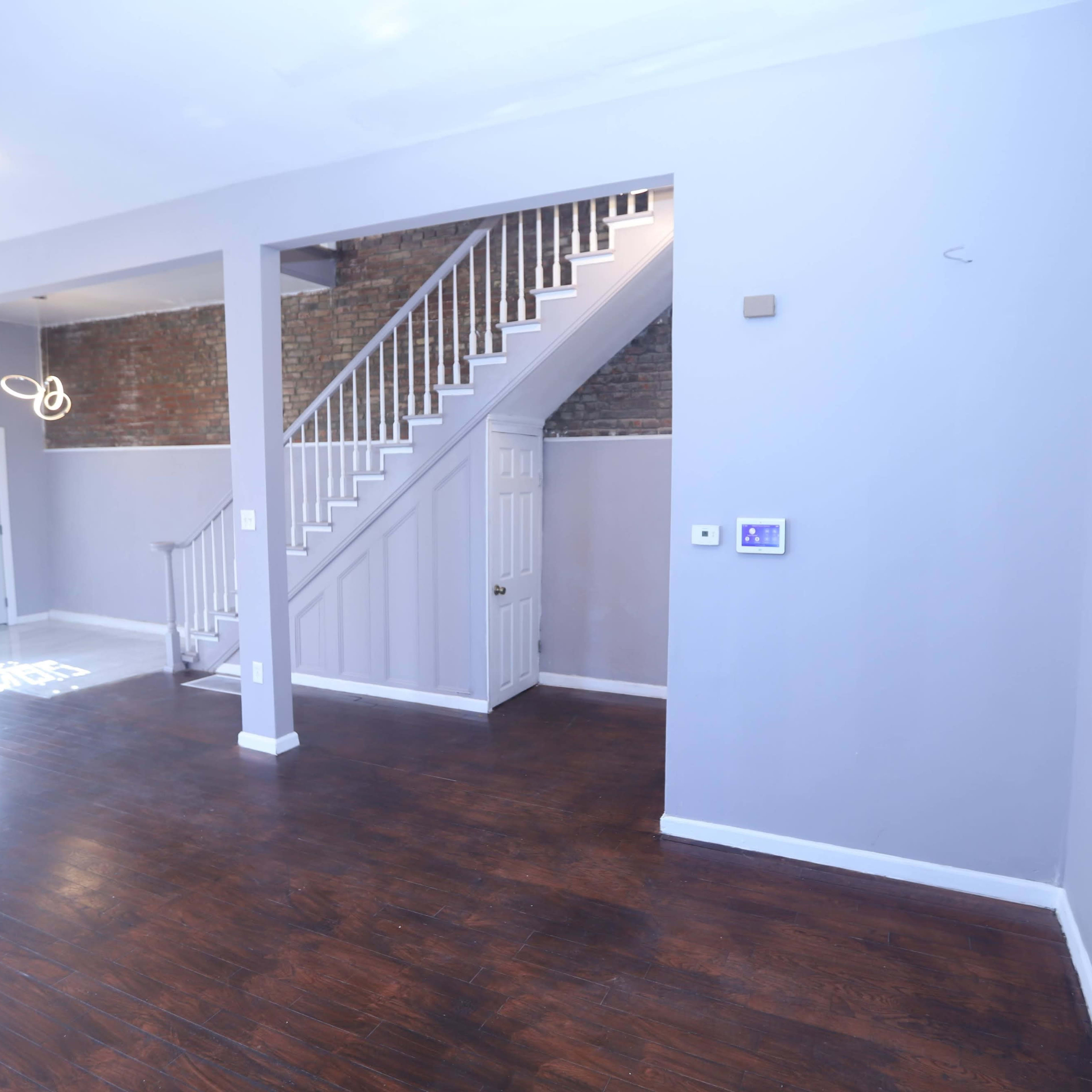 A spacious interior with wooden flooring, featuring a staircase, a door to the left, and gray walls.
