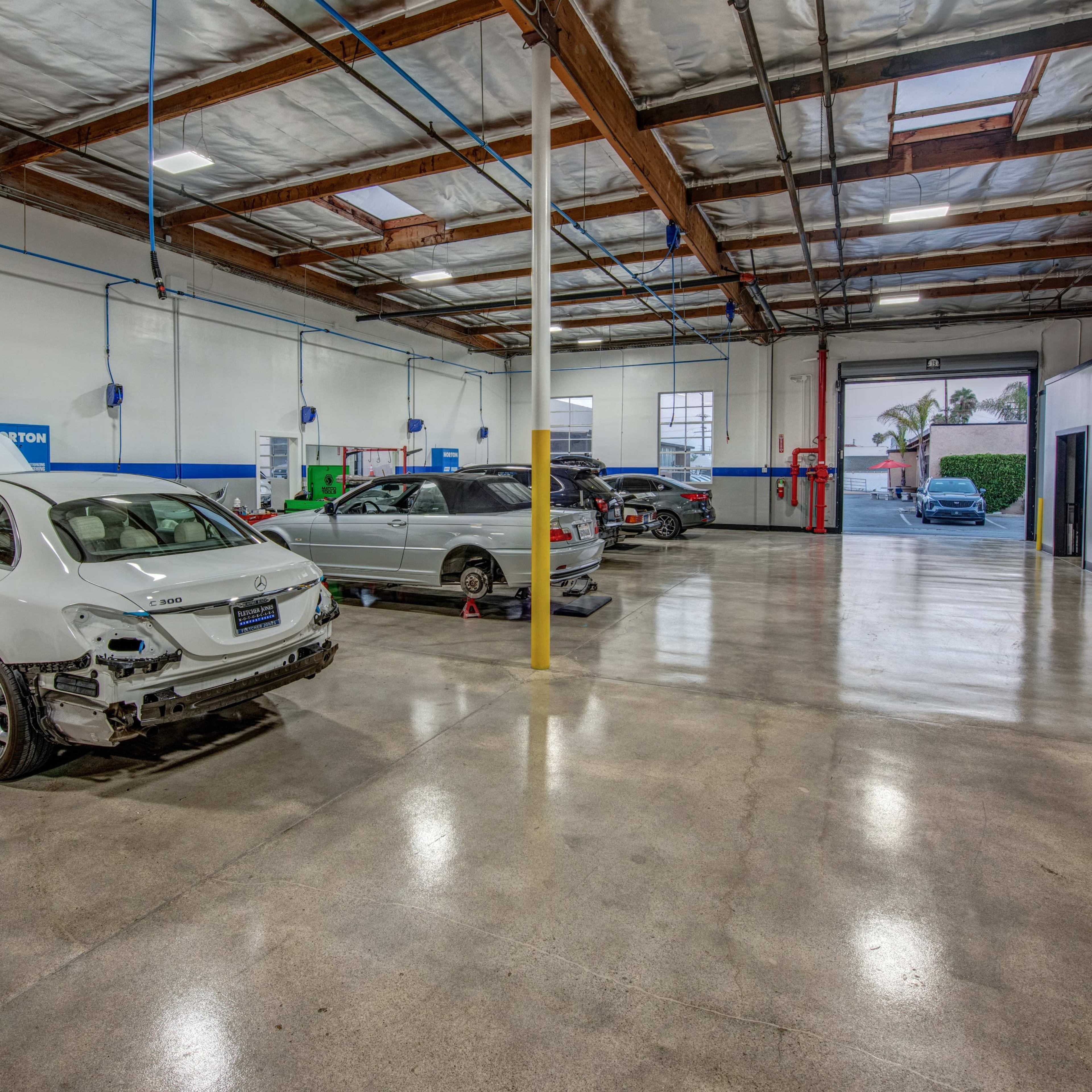 A spacious automotive repair shop with several vehicles, including a white sedan and a minivan, parked inside.