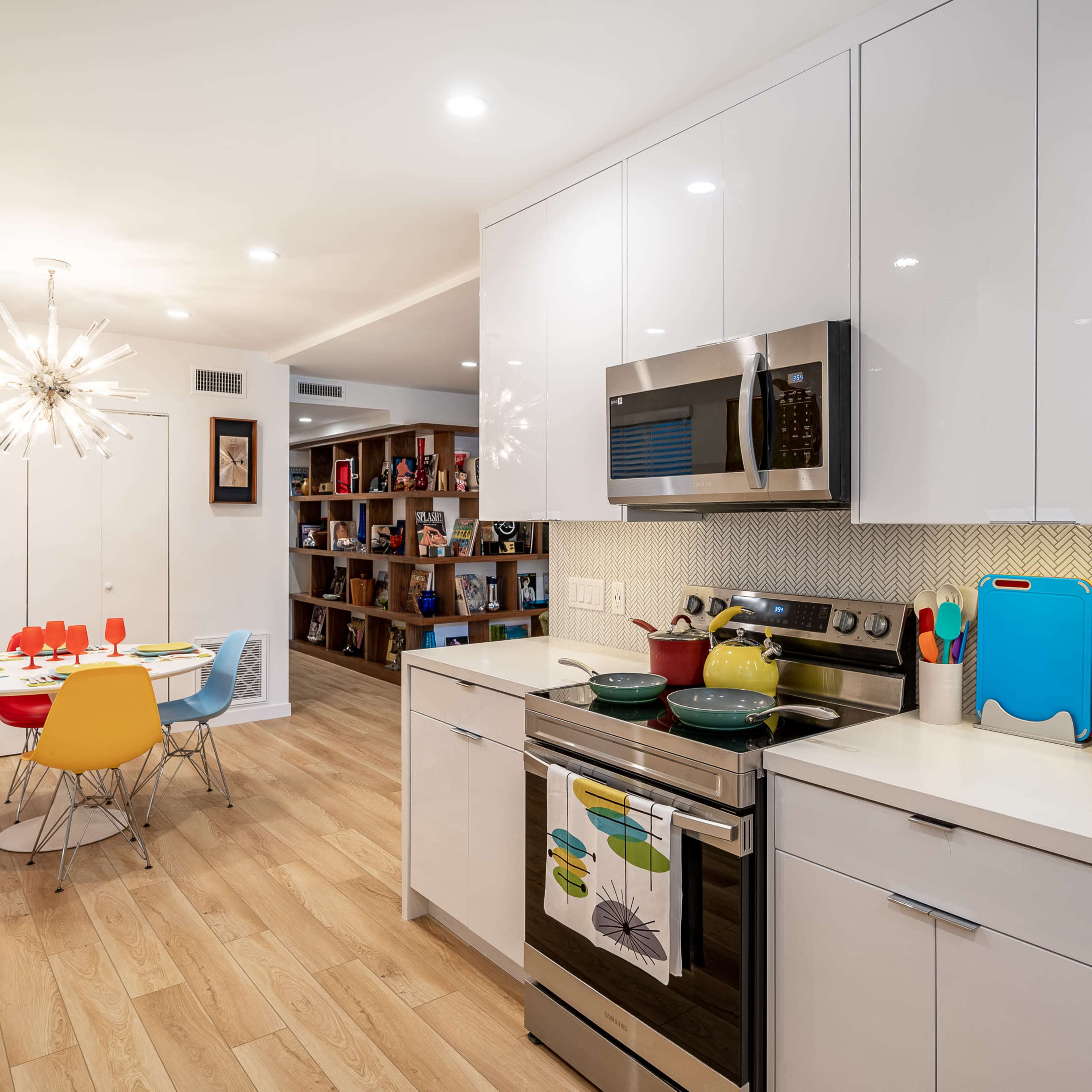 A modern kitchen with stainless steel appliances, white cabinetry, and a dining area featuring a round table surrounded by colorful chairs.
