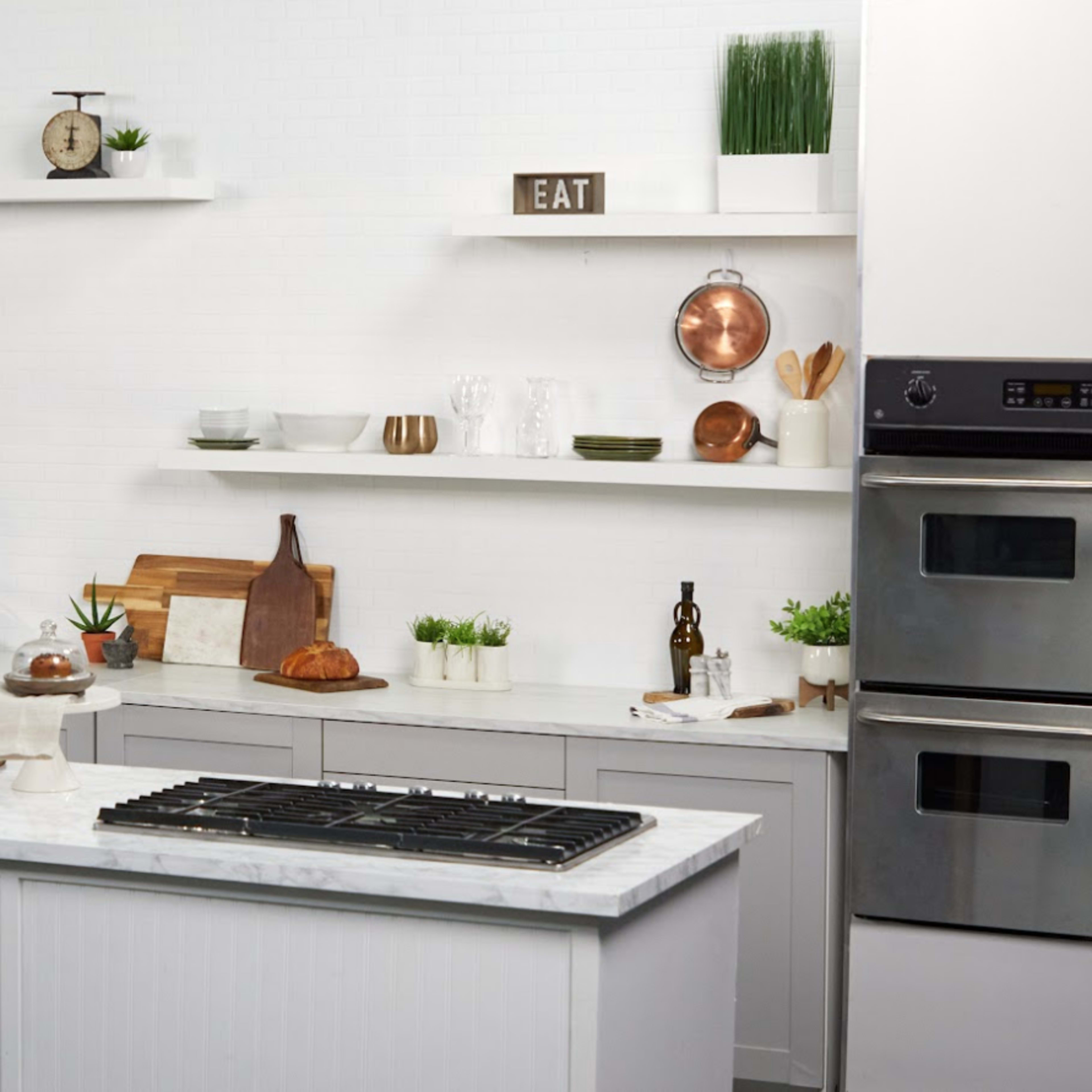 The kitchen features white walls and shelves adorned with various decorative items, a central island with a marble countertop, and stainless steel appliances.