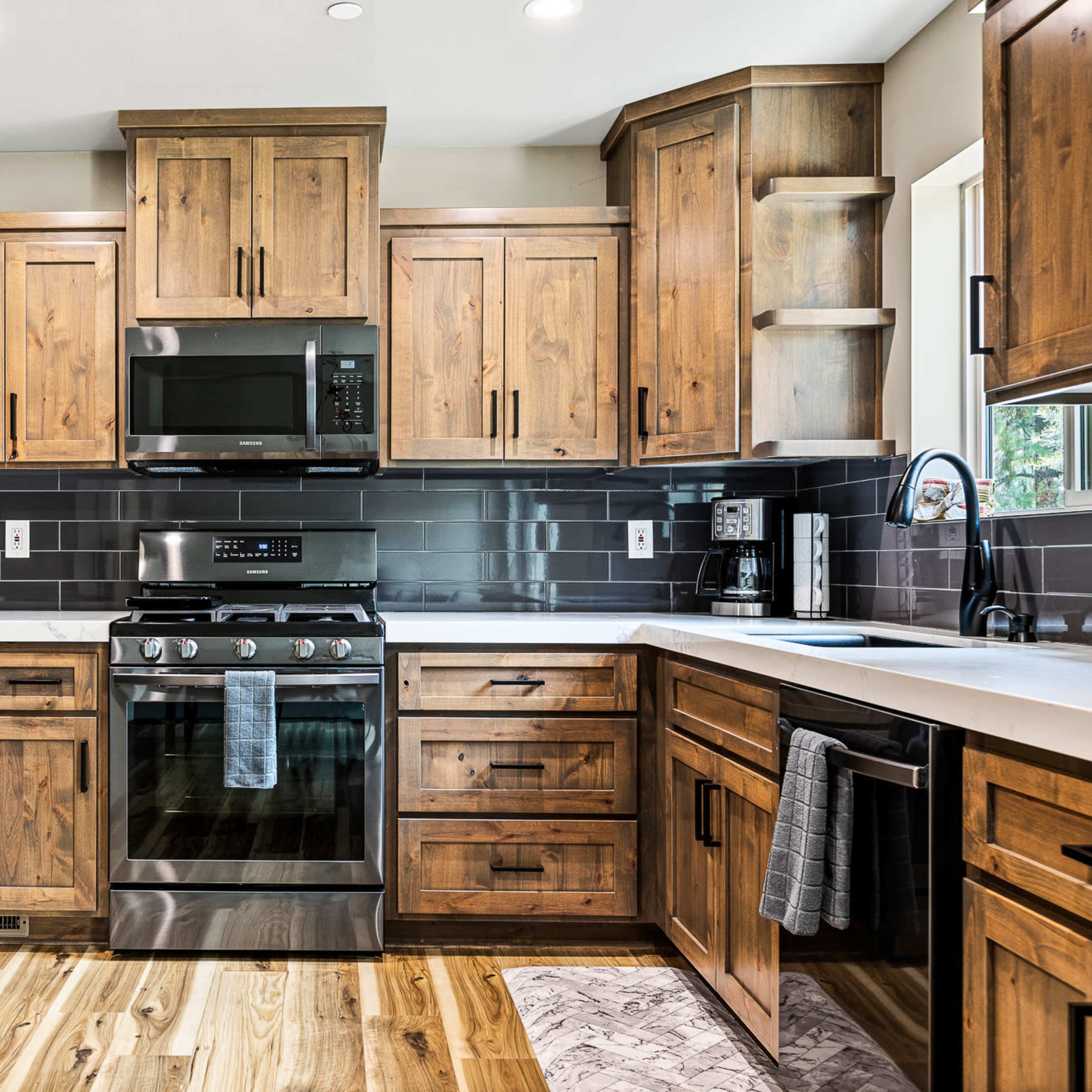 A modern kitchen features wooden cabinets, stainless steel appliances, and a contrasting dark tile backsplash.