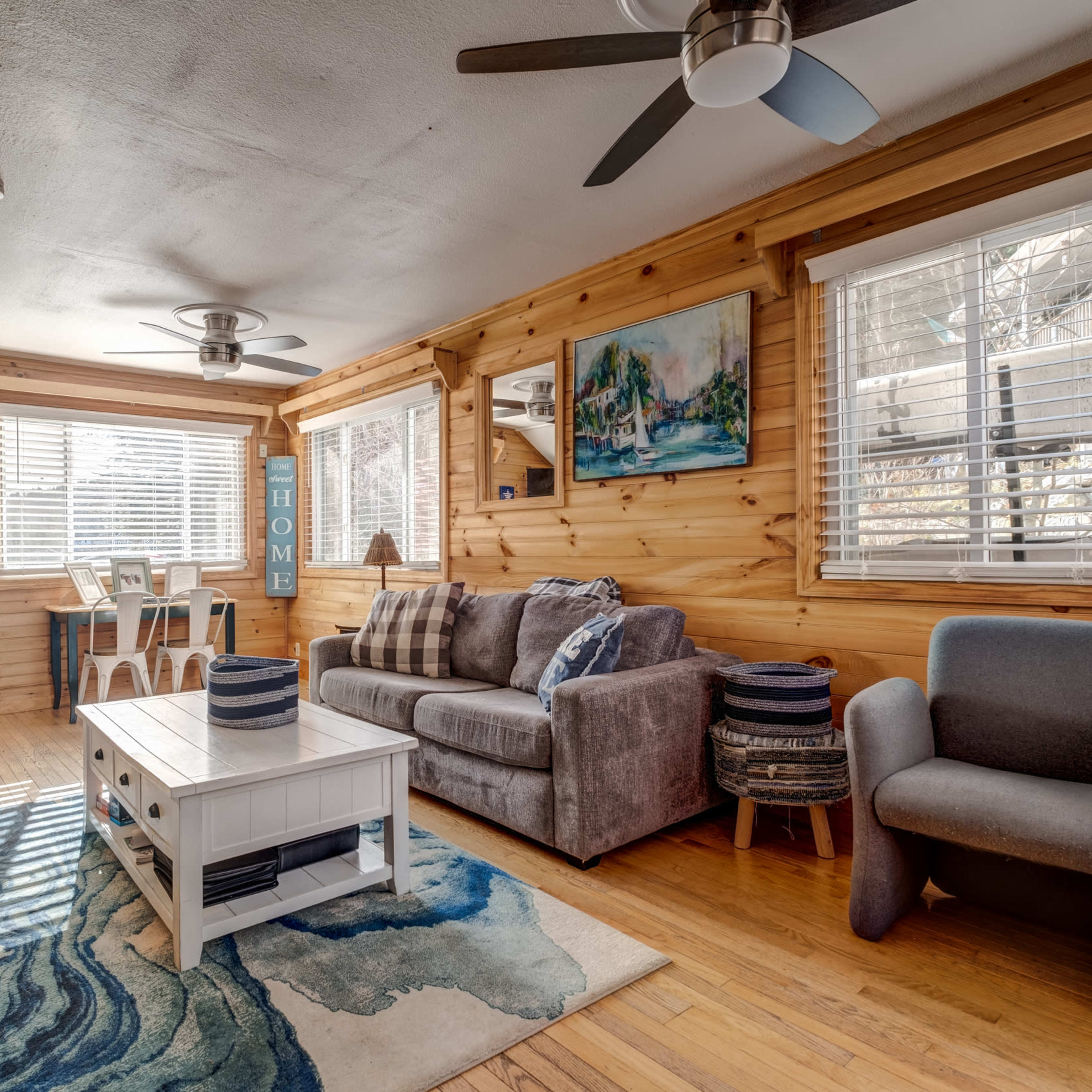 The living room features wooden walls, a sofa, a coffee table, and a dining area with a set of chairs and table beside a window.