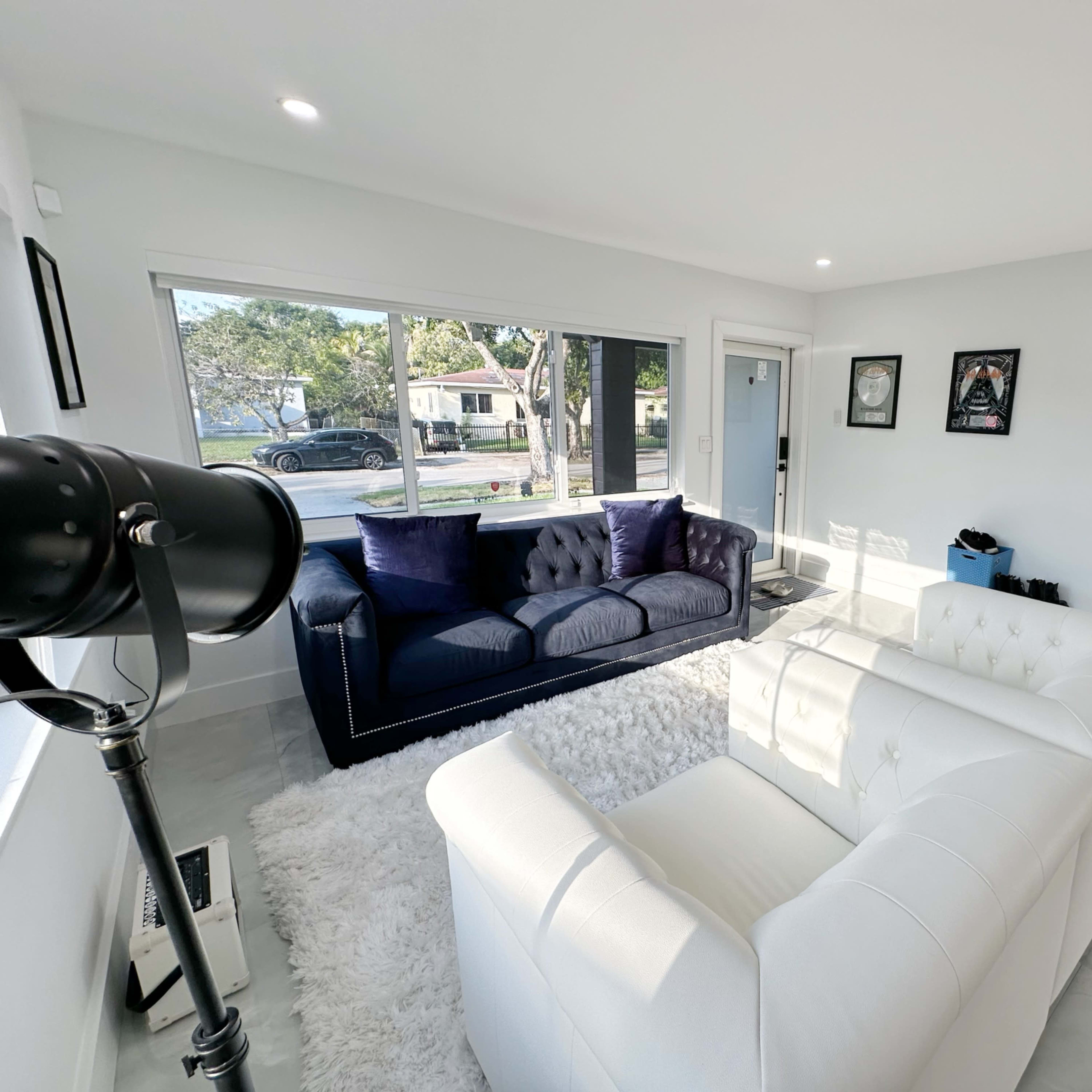 The living room features a white chesterfield sofa, a dark blue couch, and a shag rug, all illuminated by natural light from large windows.