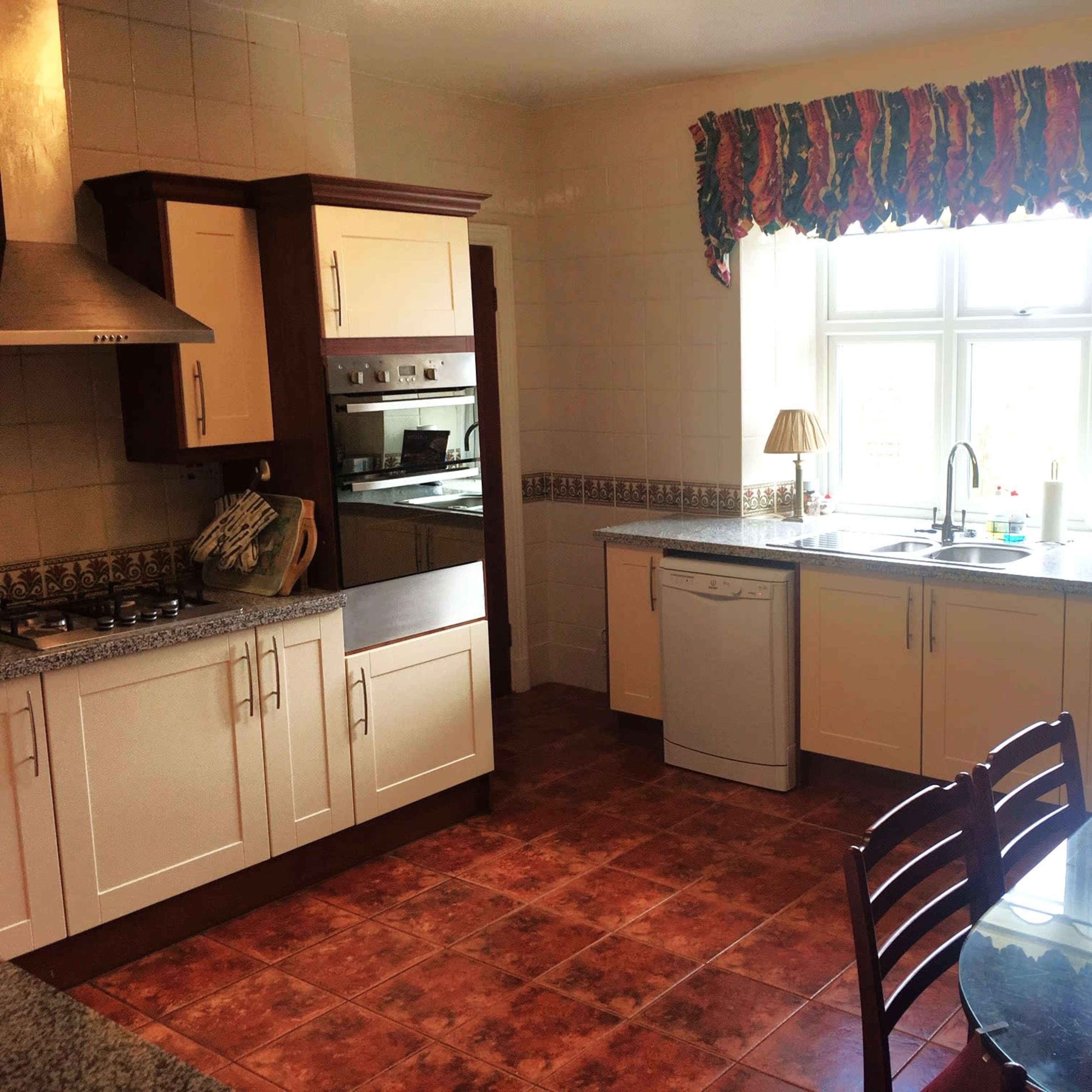 The kitchen features wooden cabinets, a countertop, a sink under a window, and a dining table nearby.
