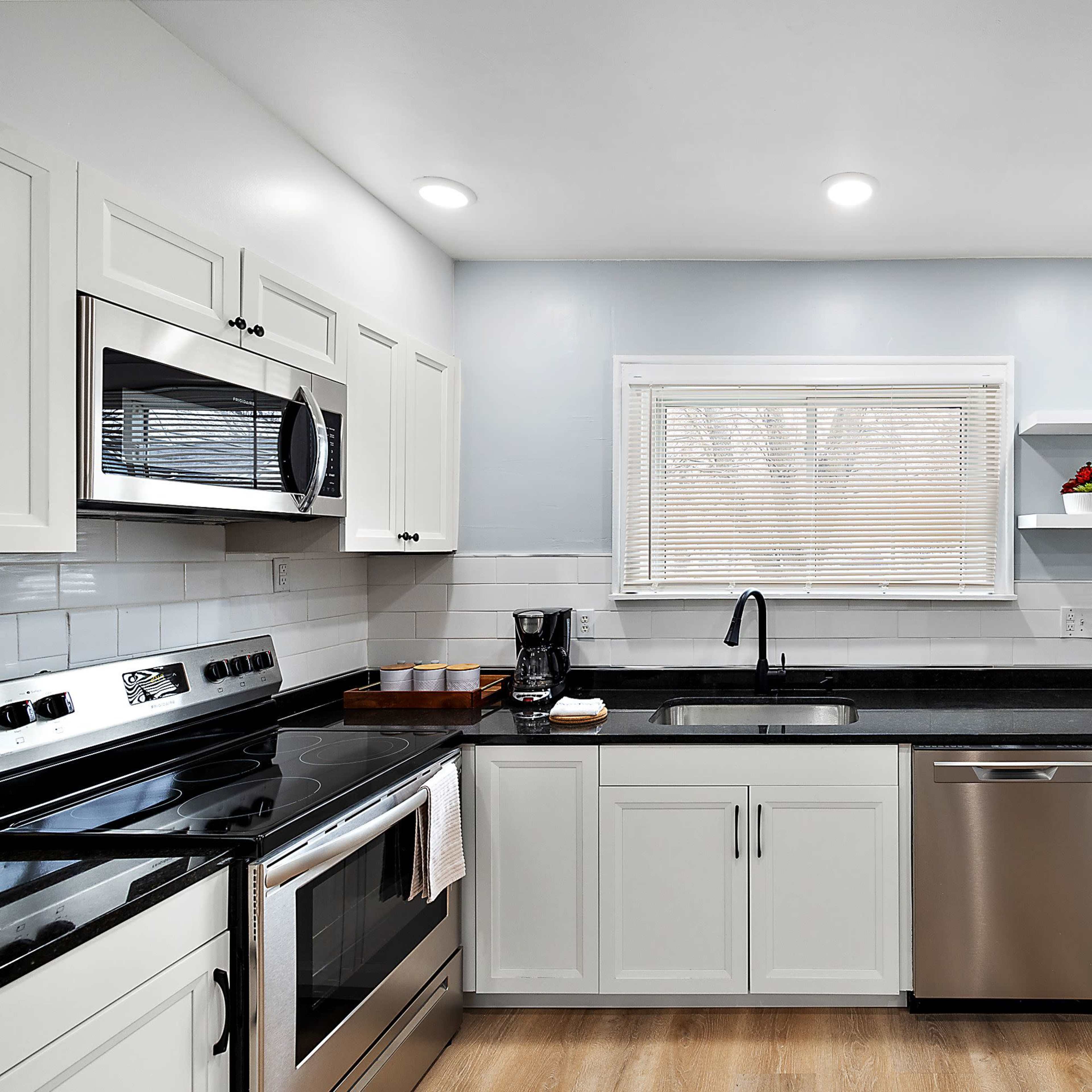 A modern kitchen with white cabinets, stainless steel appliances, a black countertop, and natural light filtering through a window.