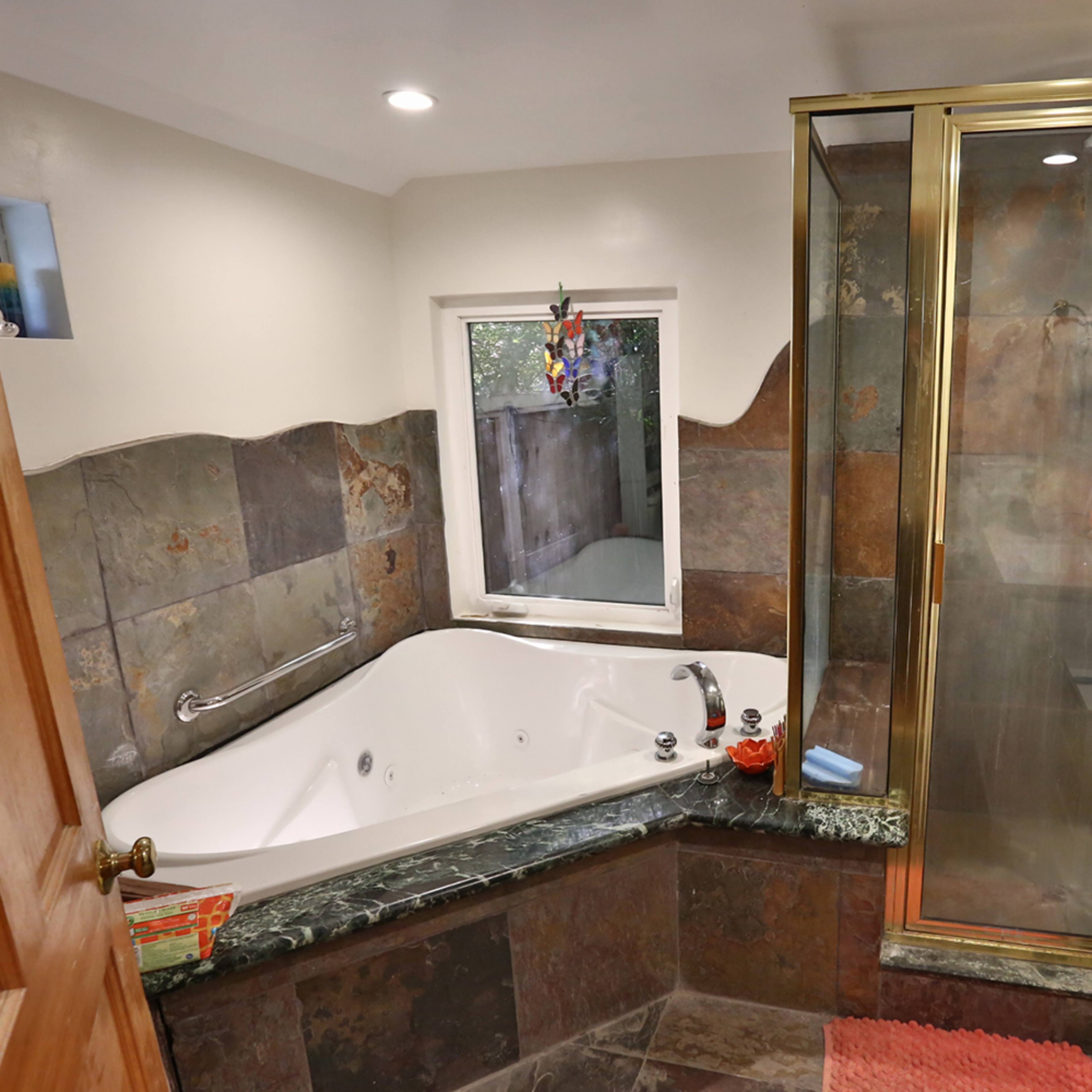 A bathroom featuring a large whirlpool tub, a glass-enclosed shower, and a stone tile design on the walls and floor.