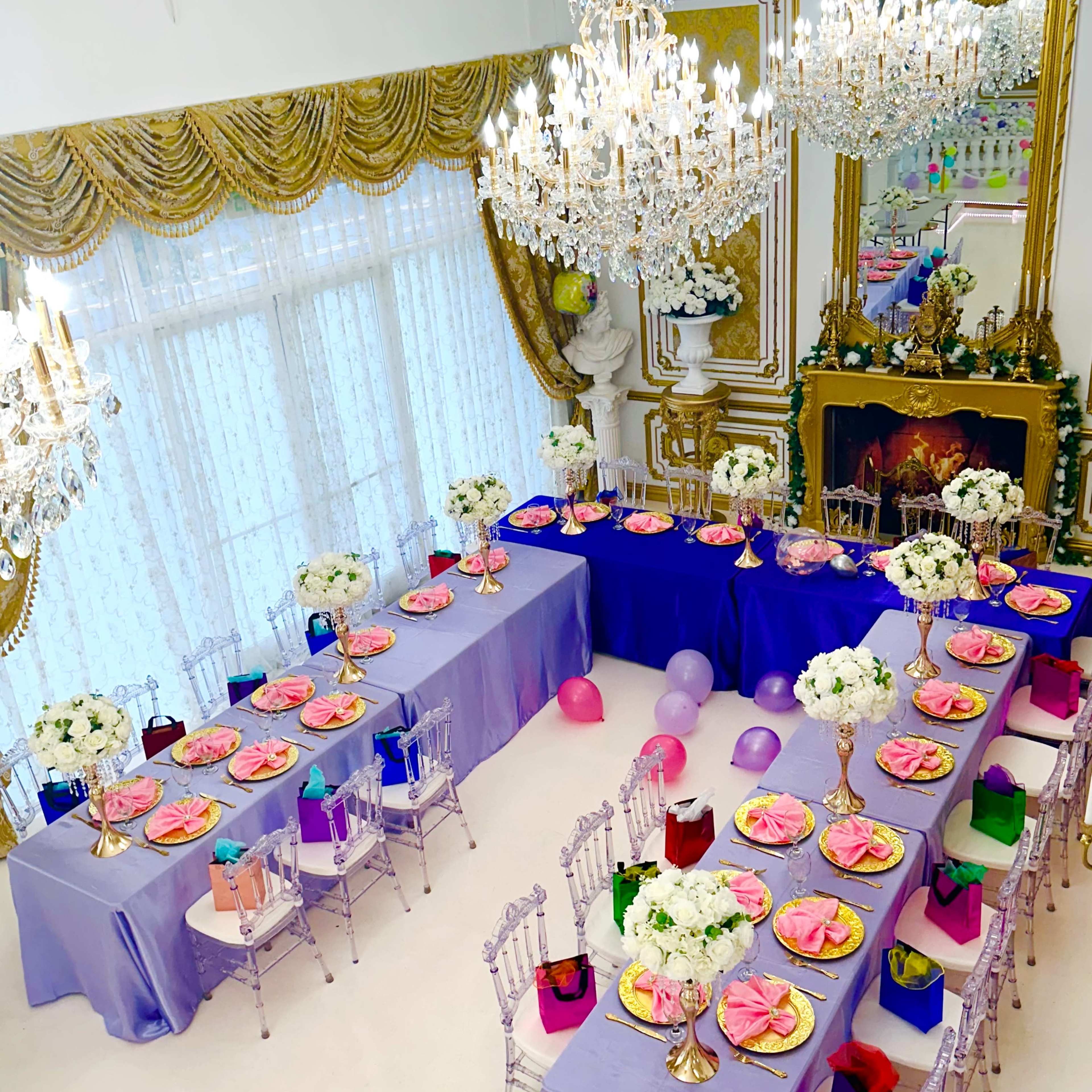 A lavishly decorated dining room features elegantly set tables with floral centerpieces, colorful plates, and chandeliers hanging from the ceiling.