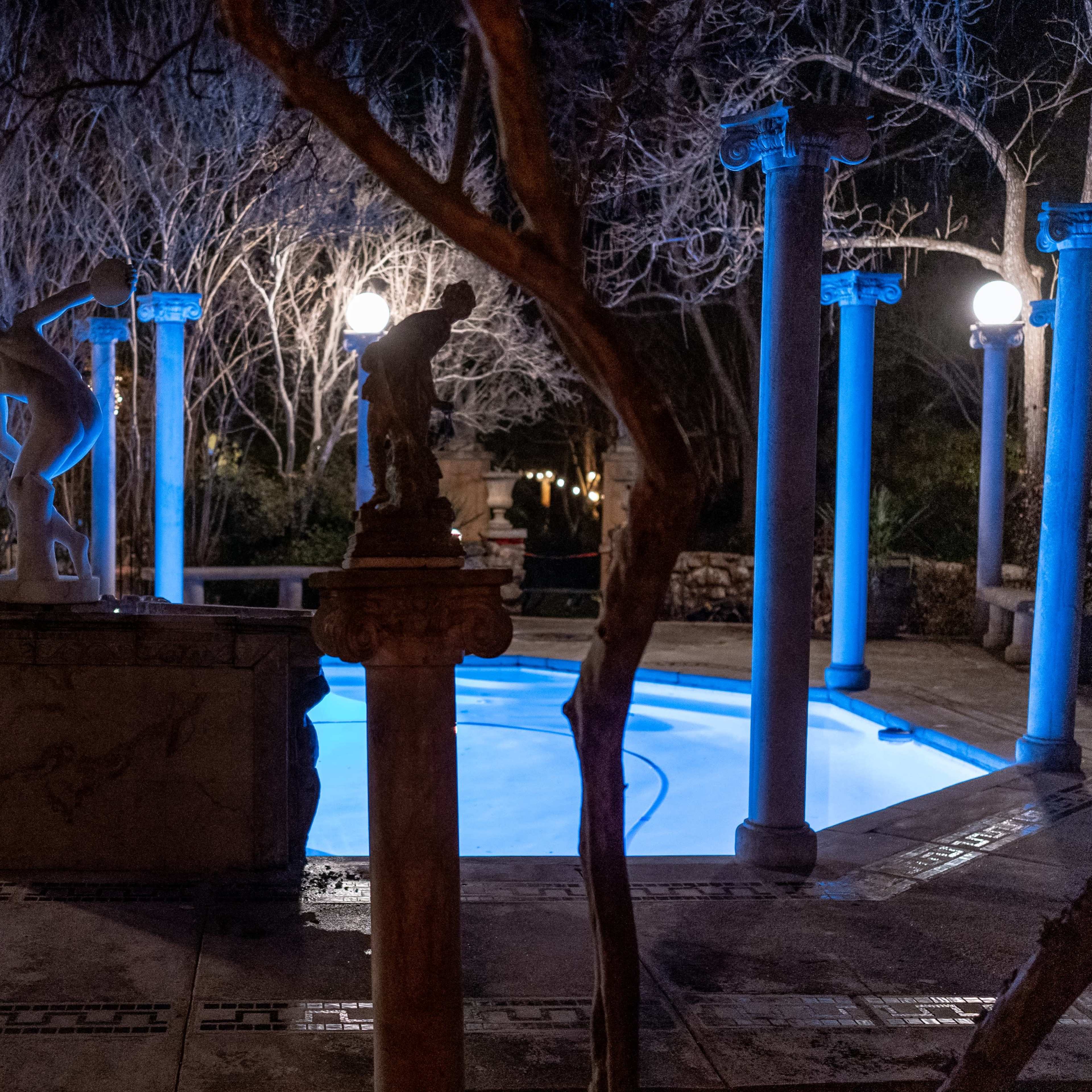 A illuminated circular pool surrounded by columns, with sculptures and dim lighting in a tranquil nighttime setting.