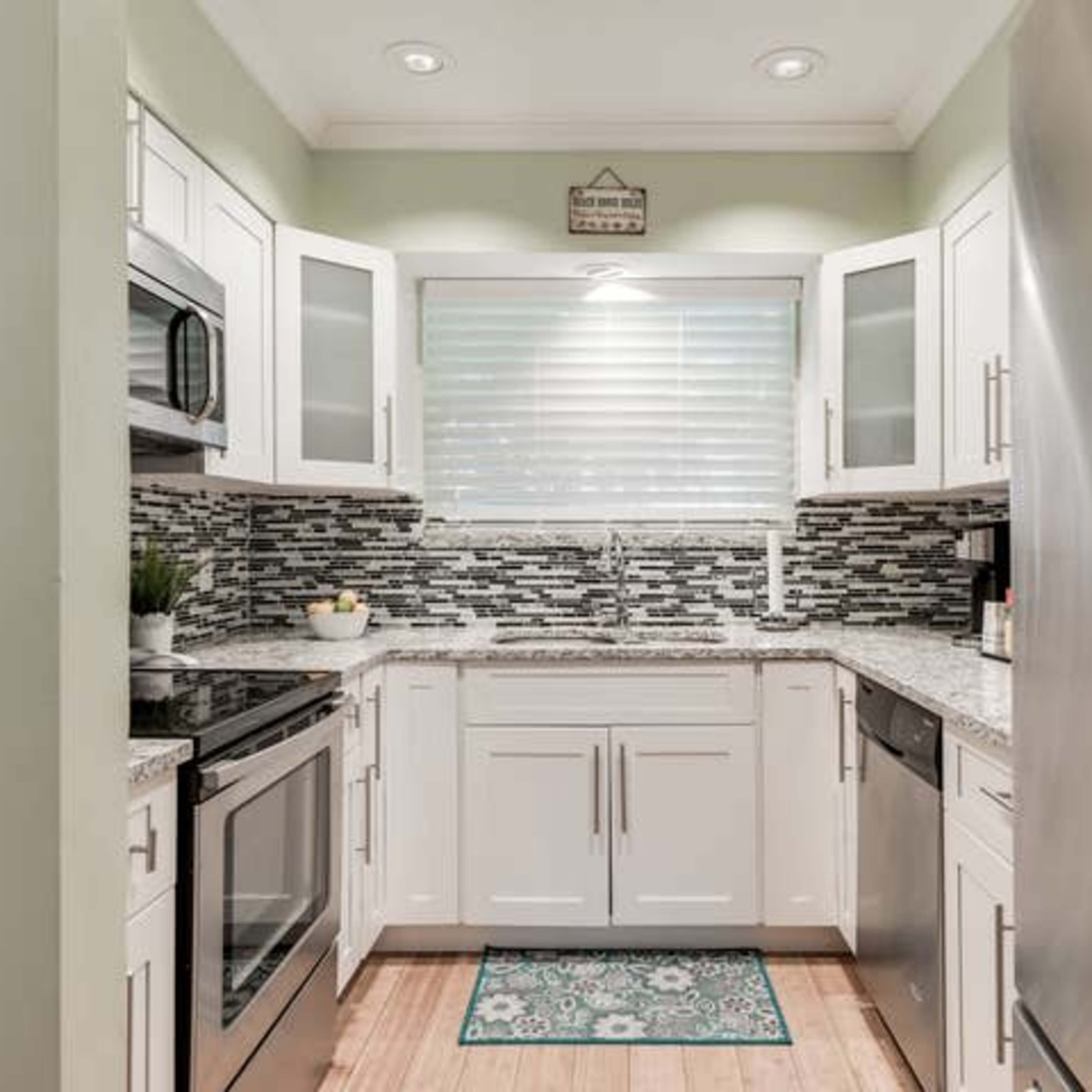 A modern kitchen features white cabinetry, a stainless steel refrigerator, and a mosaic tile backsplash.