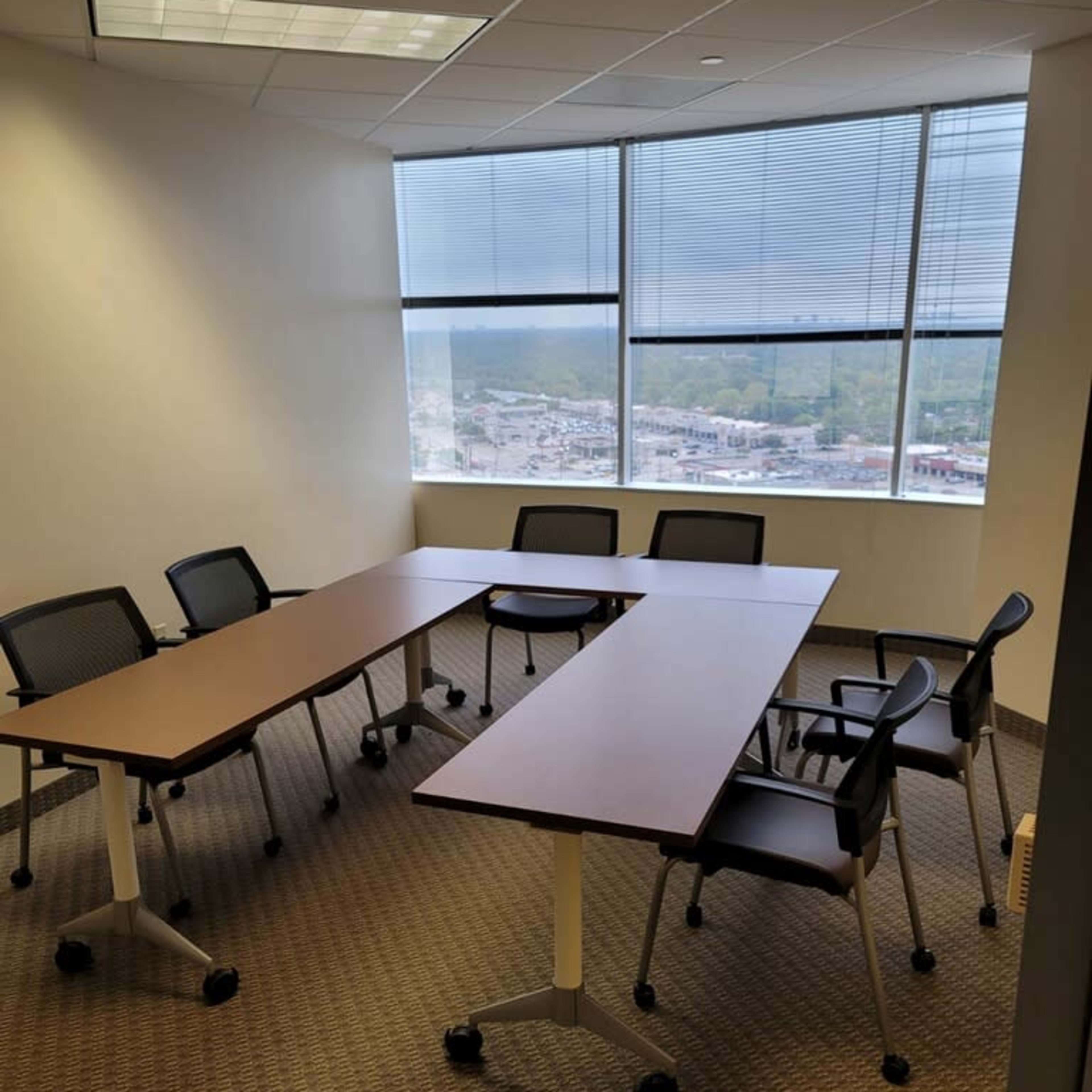 A conference room with a large table and several rolling chairs is set up near a window overlooking the outside.