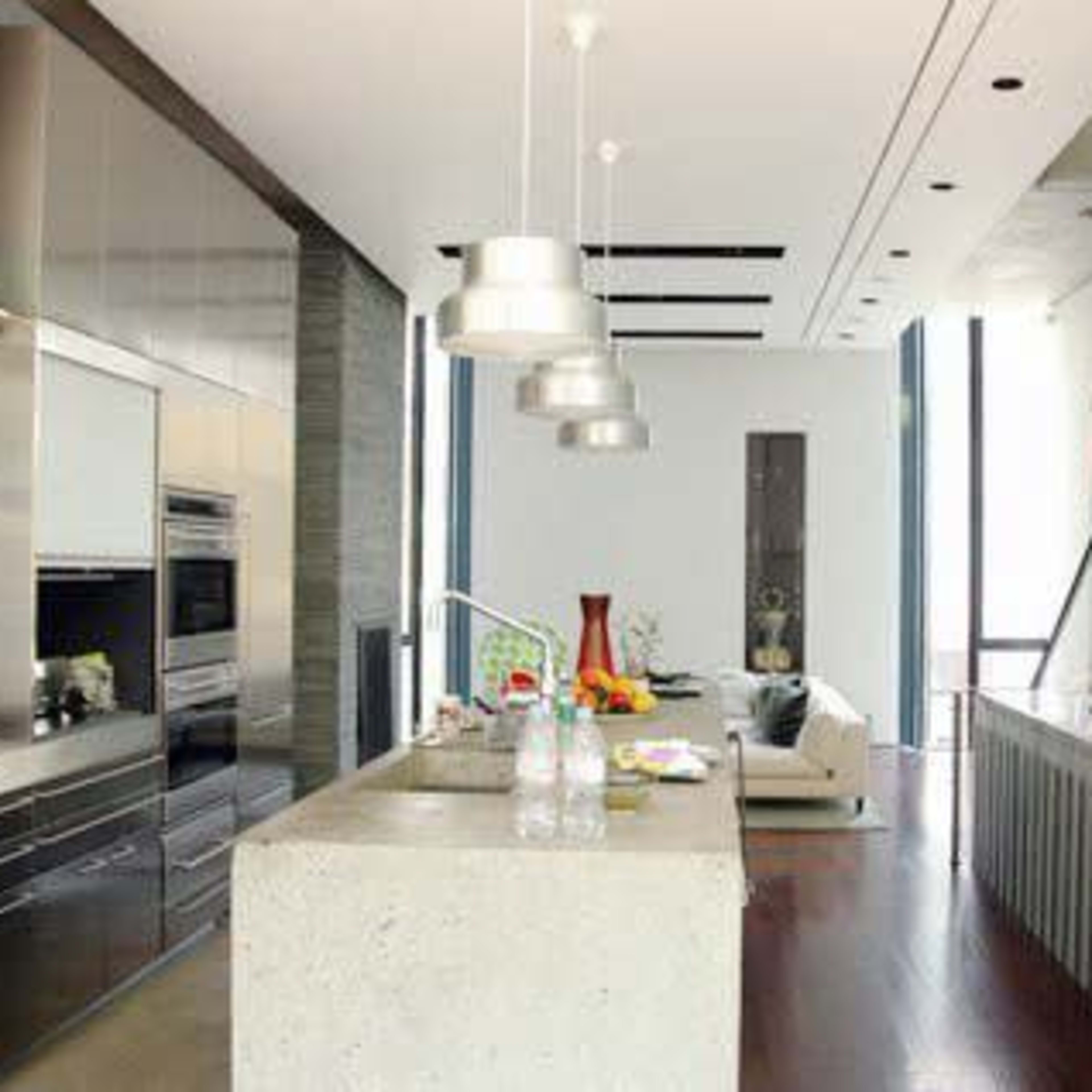 A modern kitchen with a concrete island and stainless steel appliances, adjacent to a living area and a staircase.