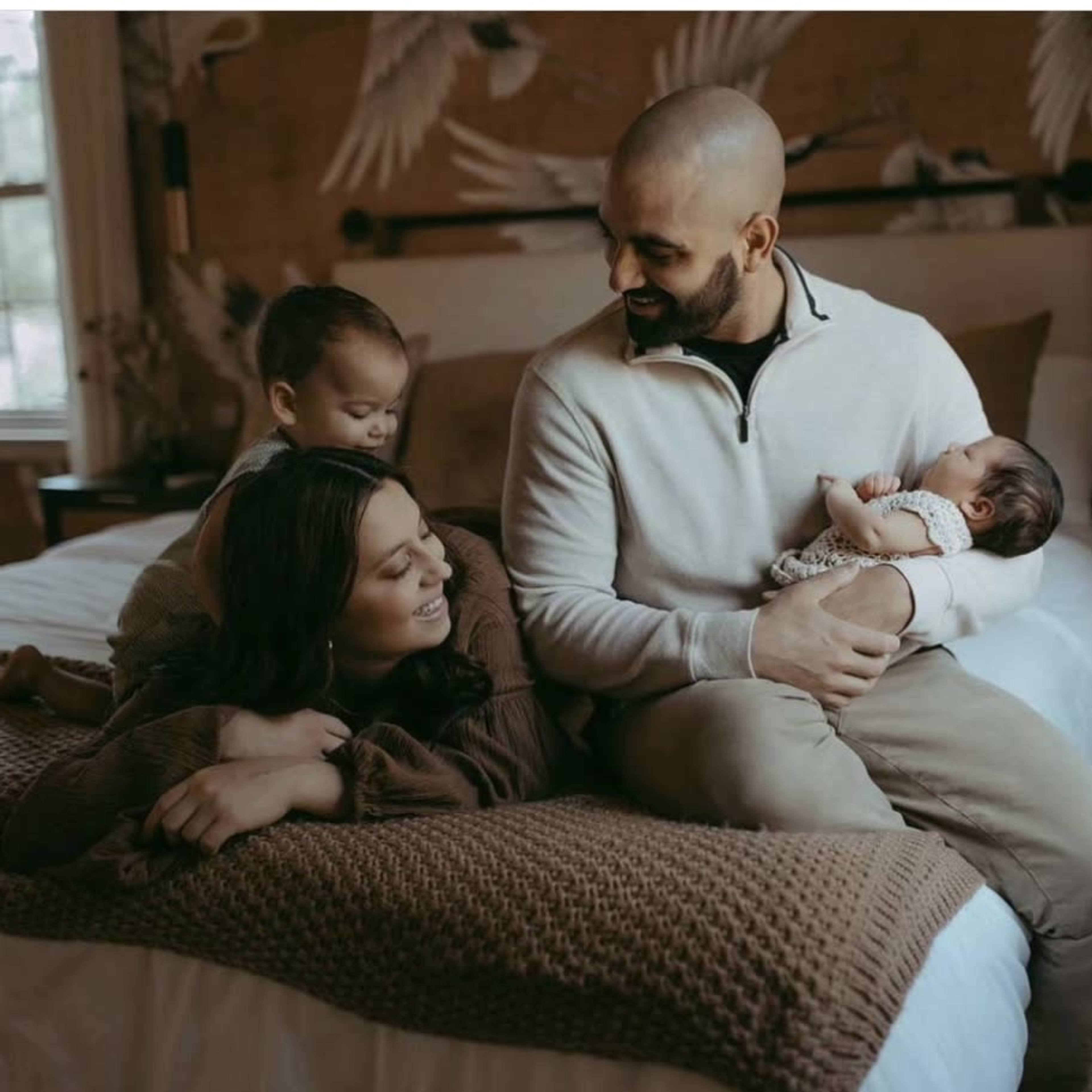 A family sits together on a bed, with two children interacting and a parent holding an infant.