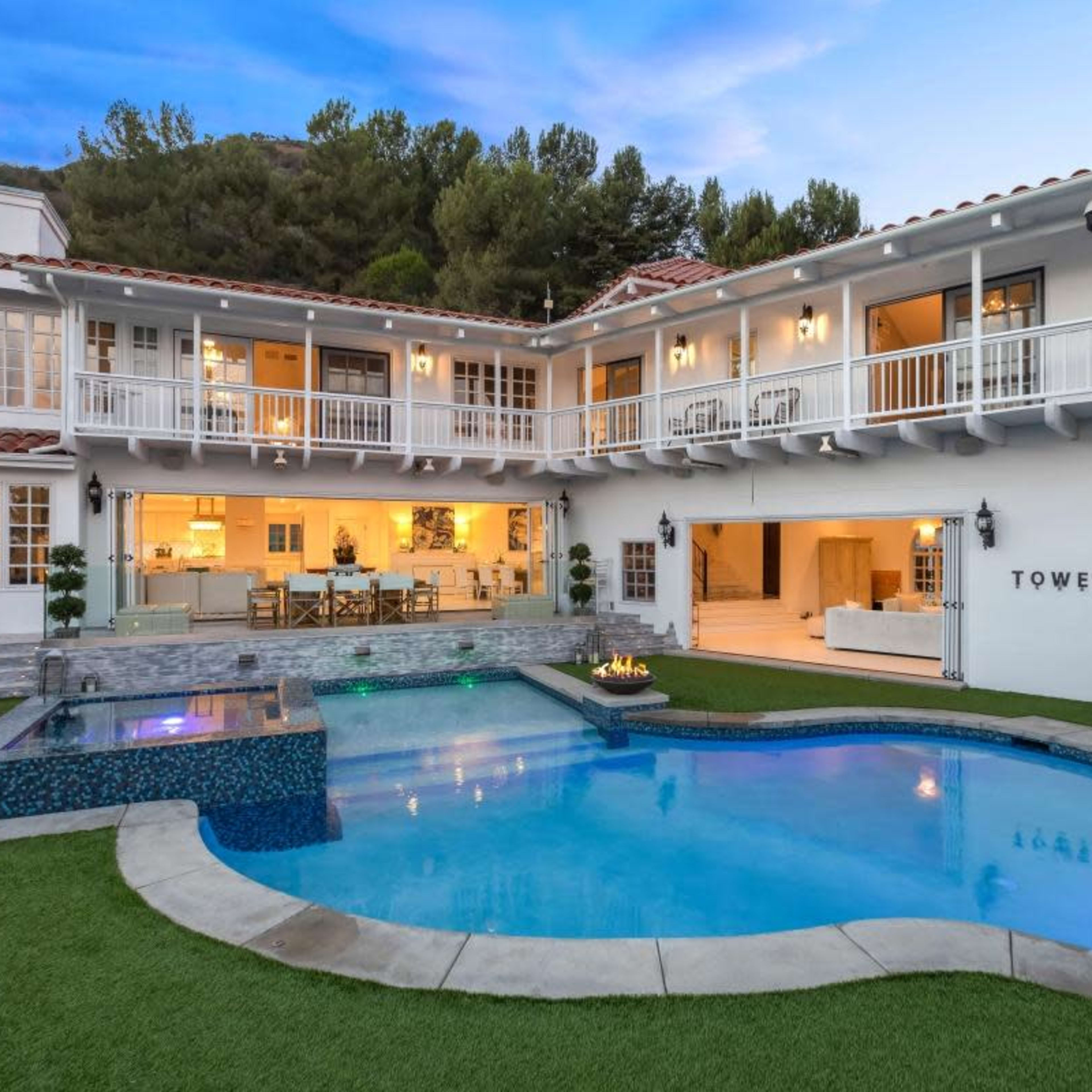 A two-story modern house with a pool and outdoor seating area, set against a hillside backdrop.