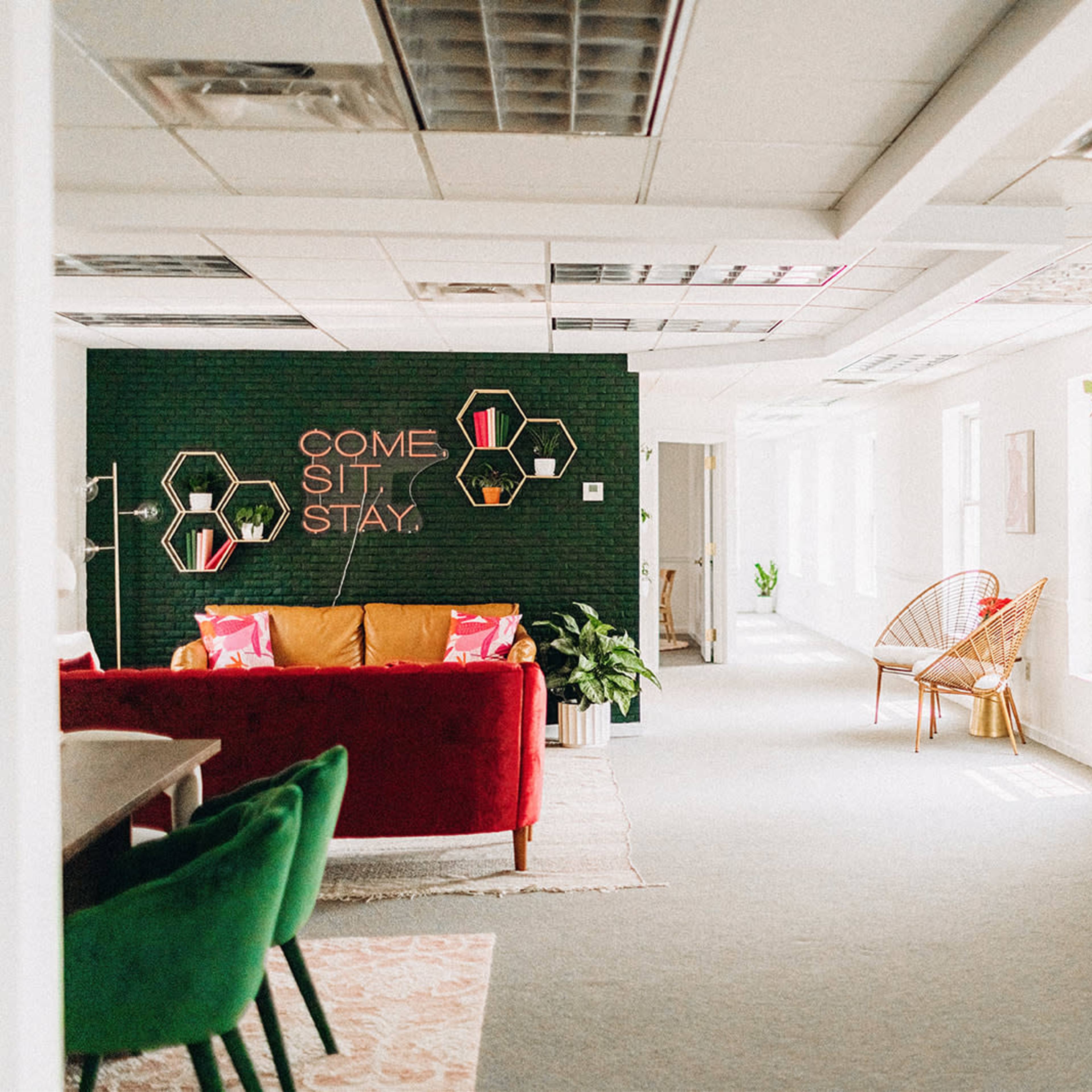 A modern office space with a bright red sofa, green accents, and decorative wall art, including a large sign that reads "WOMAN."