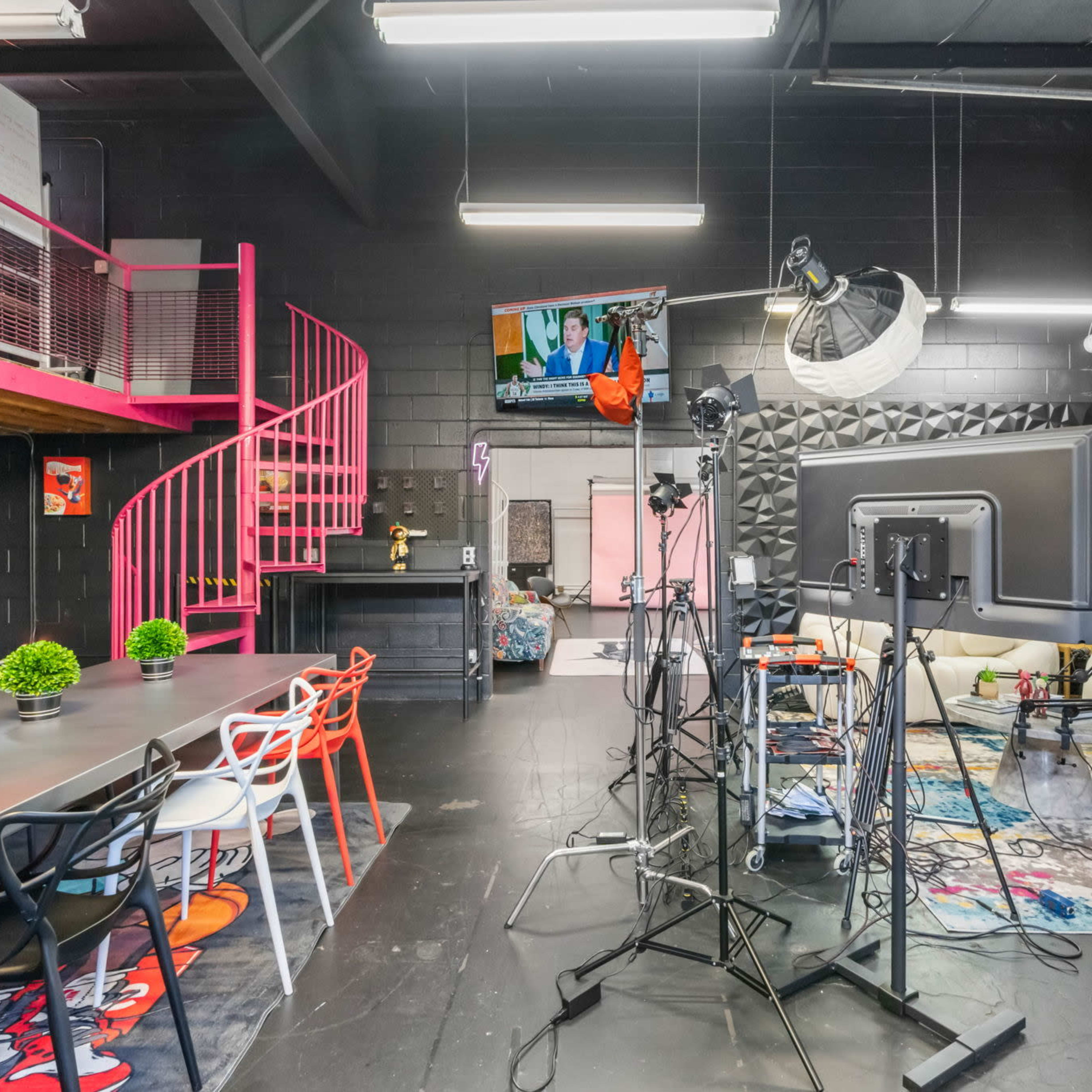 A modern studio space featuring a spiral staircase, a large screen on the wall, and various equipment set up for filming or recording.