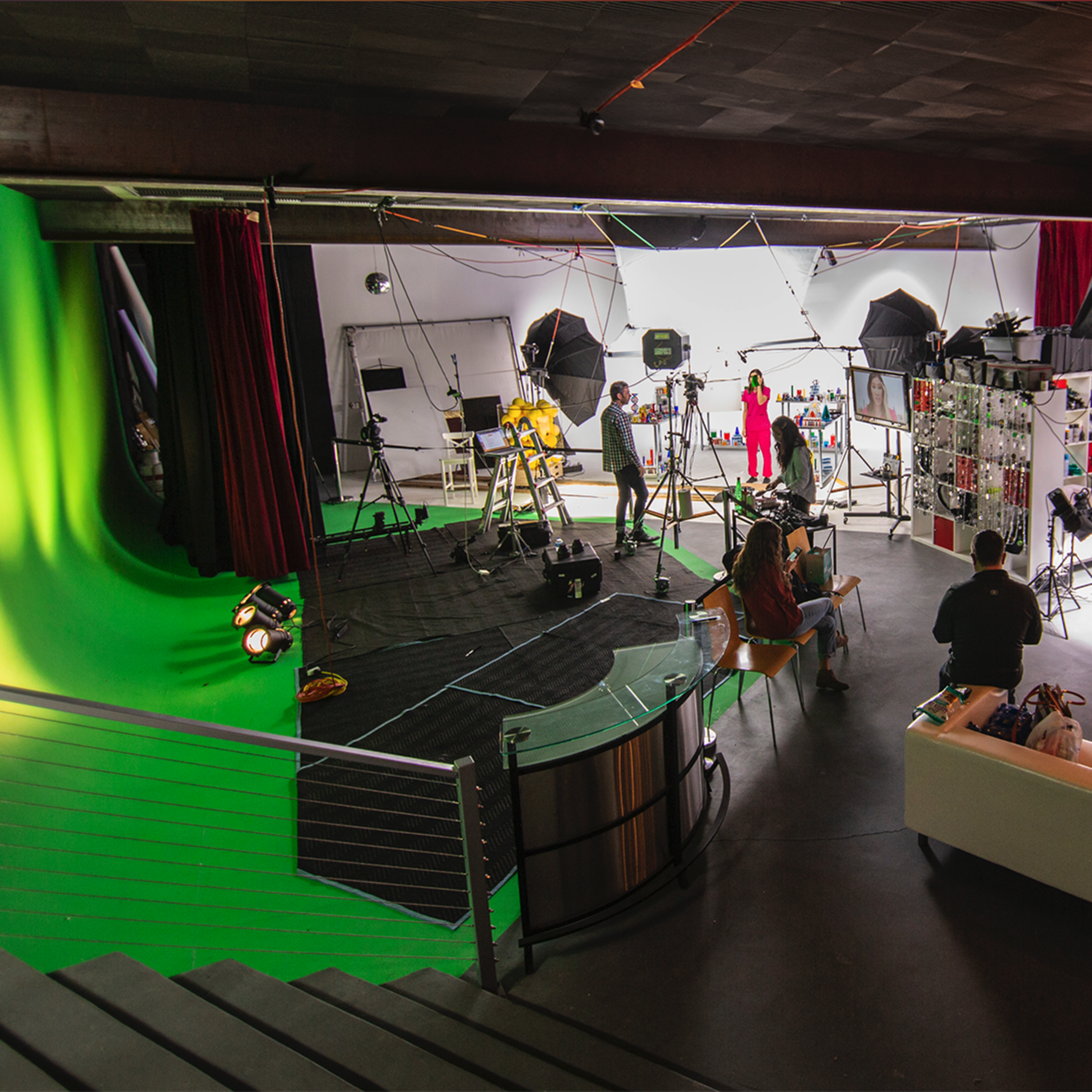 A photography studio equipped with a green screen, multiple lighting setups, and various props, with several people positioned around the space.