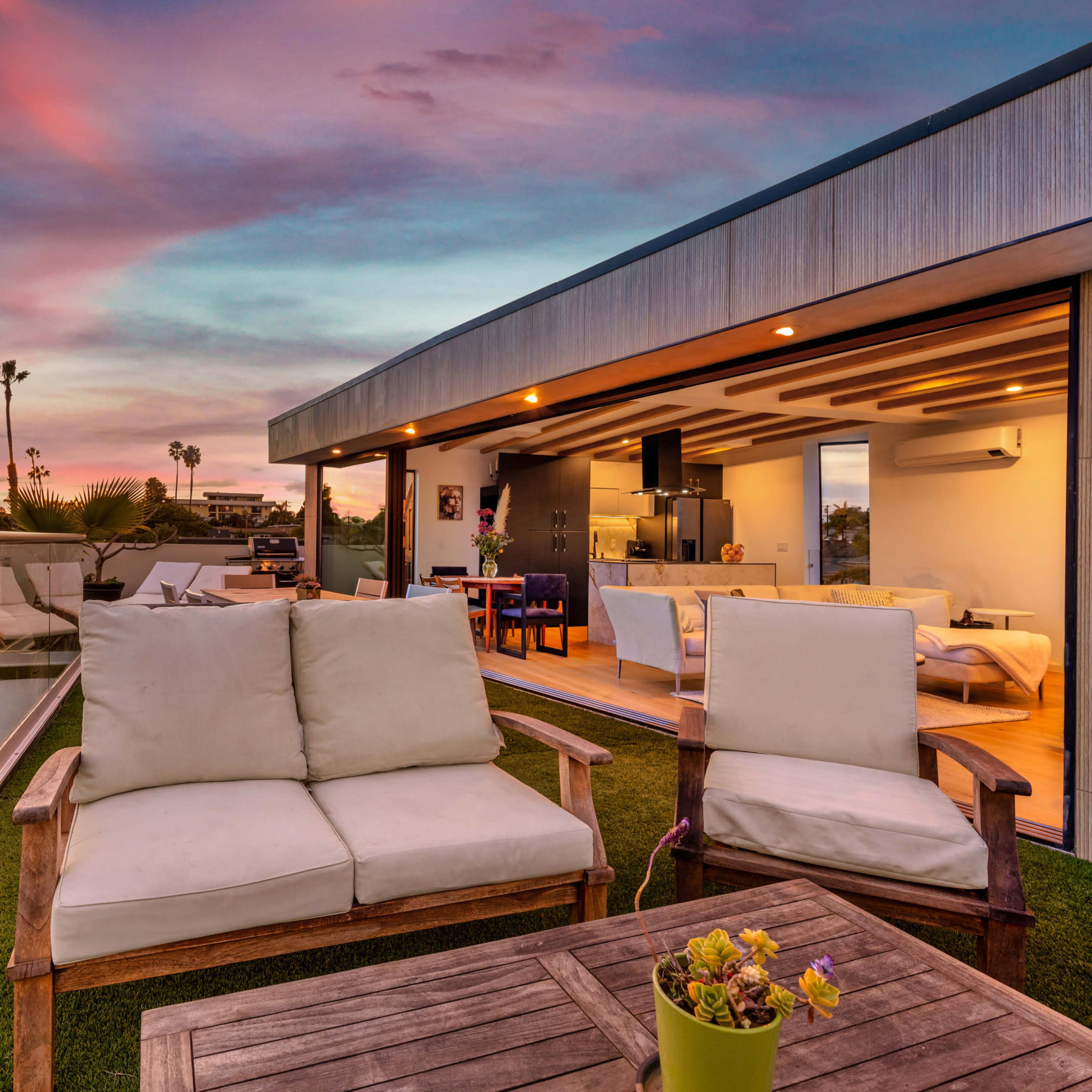 A rooftop terrace features comfortable seating and views of a vibrant sunset over a modern living space.