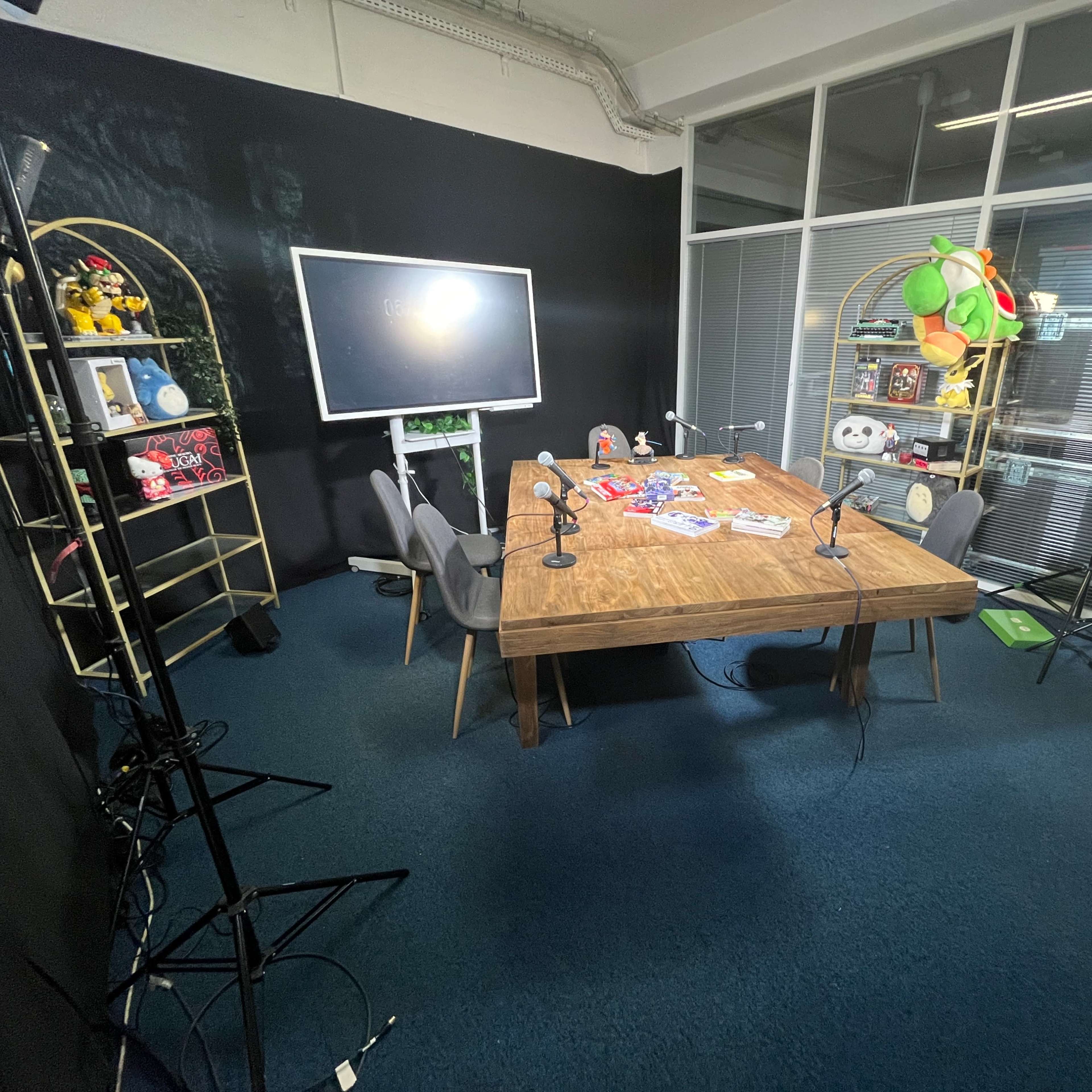 A recording studio setup with a wooden table, chairs, microphones, and various props on a dark backdrop.