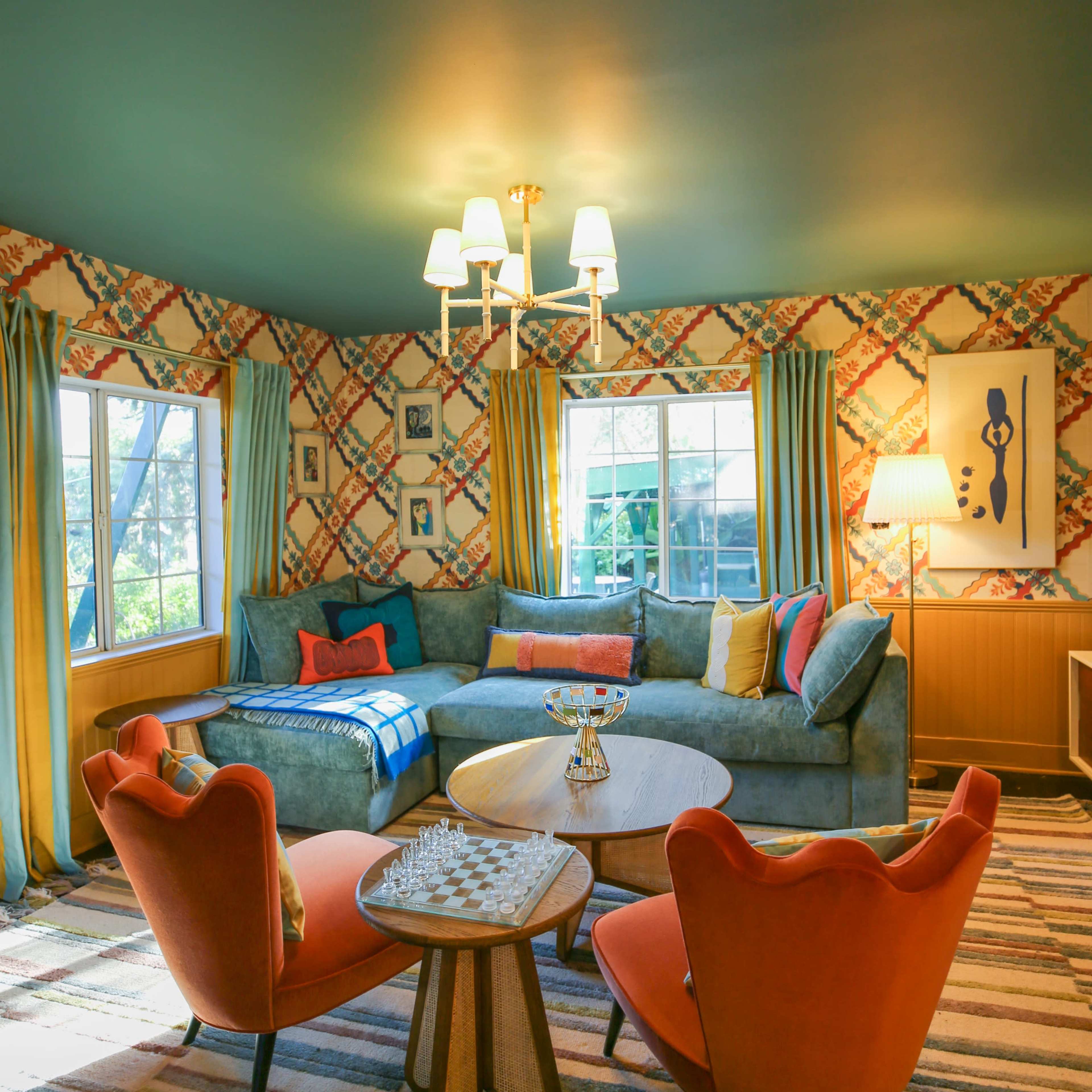 A cozy living room with a sectional sofa, an orange armchair, a round coffee table, and colorful patterned walls.