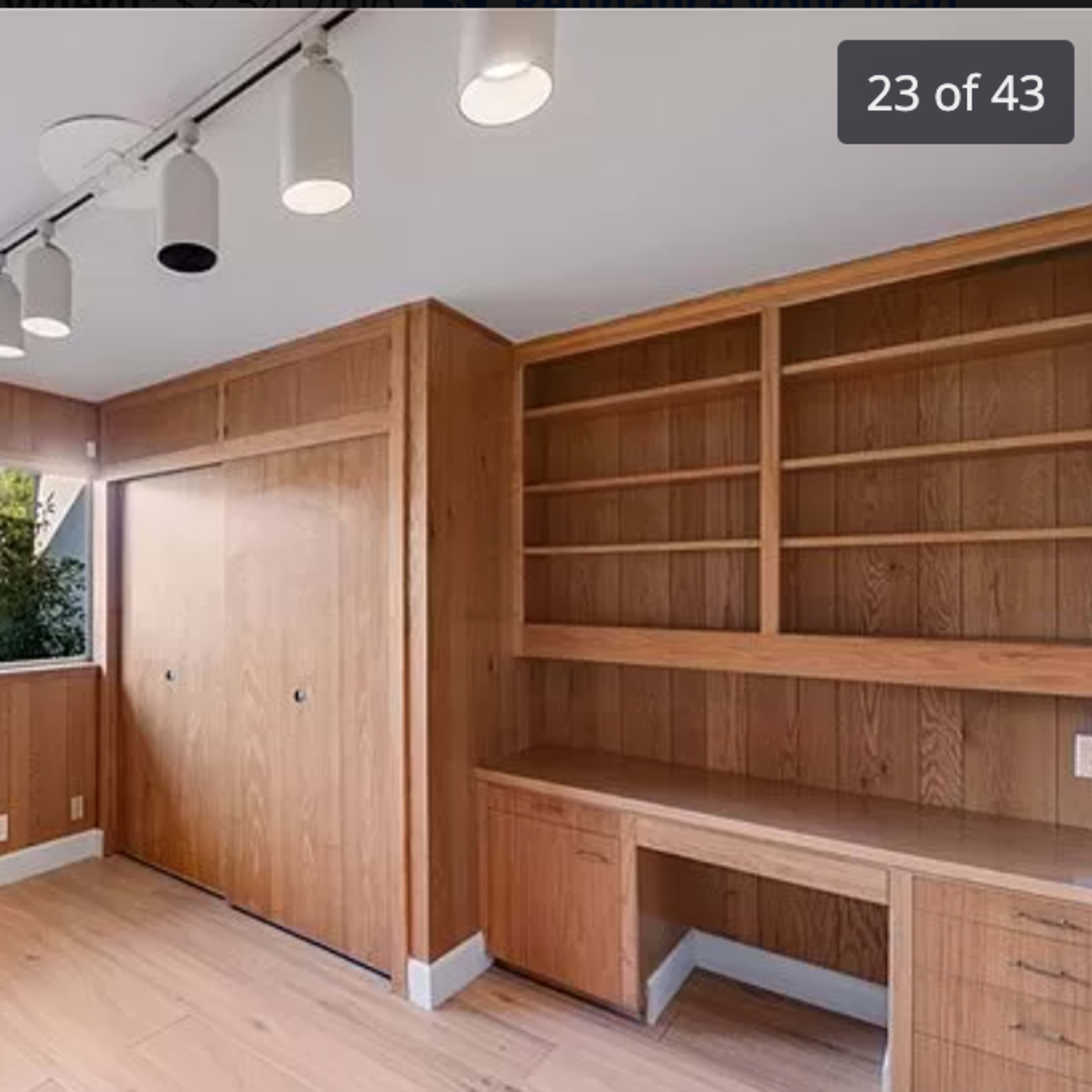 A room with wooden paneling, featuring a large window overlooking a yard, a built-in closet, and a desk area.