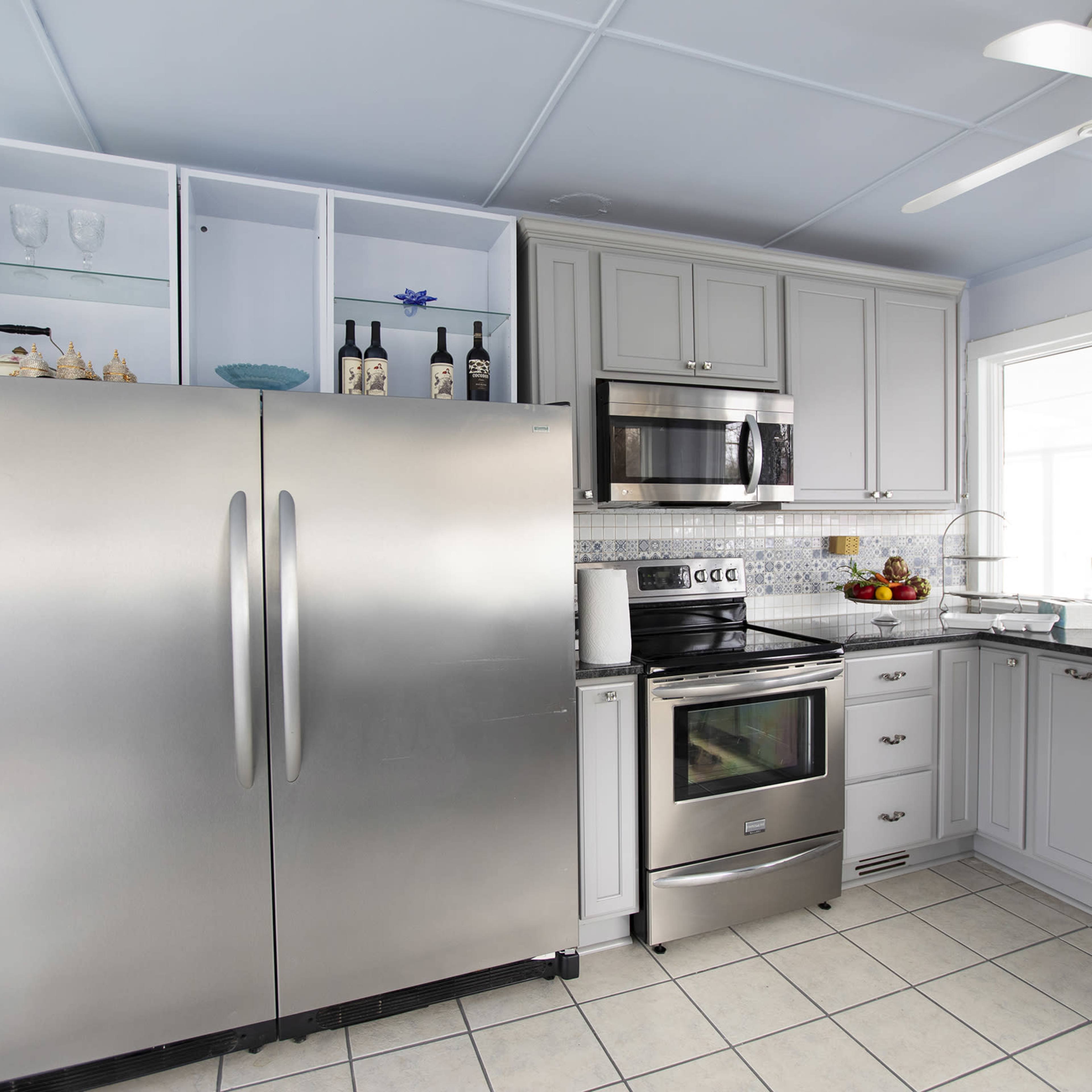 A modern kitchen with stainless steel appliances, gray cabinets, and a large window providing natural light.