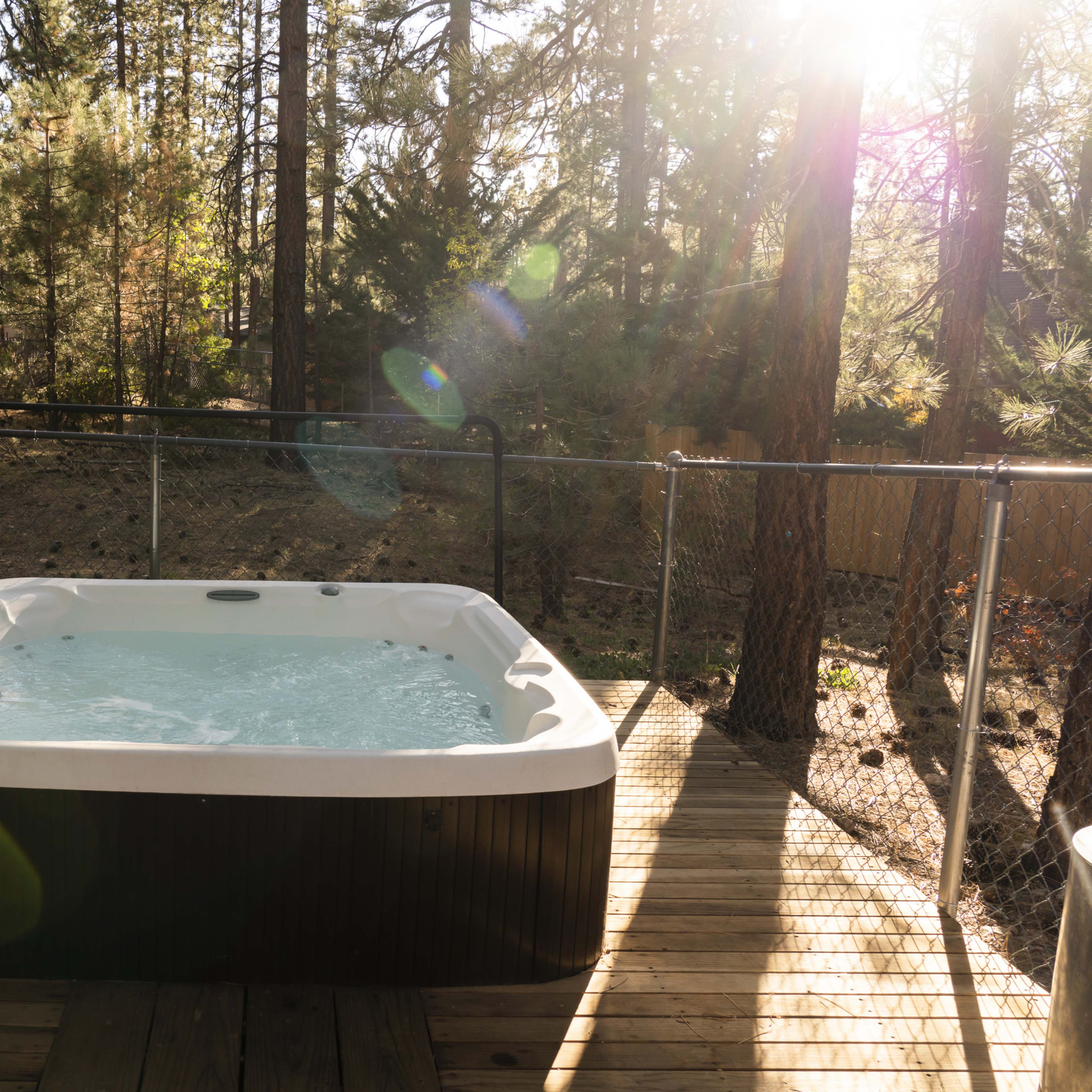 A hot tub filled with water sits on a wooden deck surrounded by trees in a backyard.