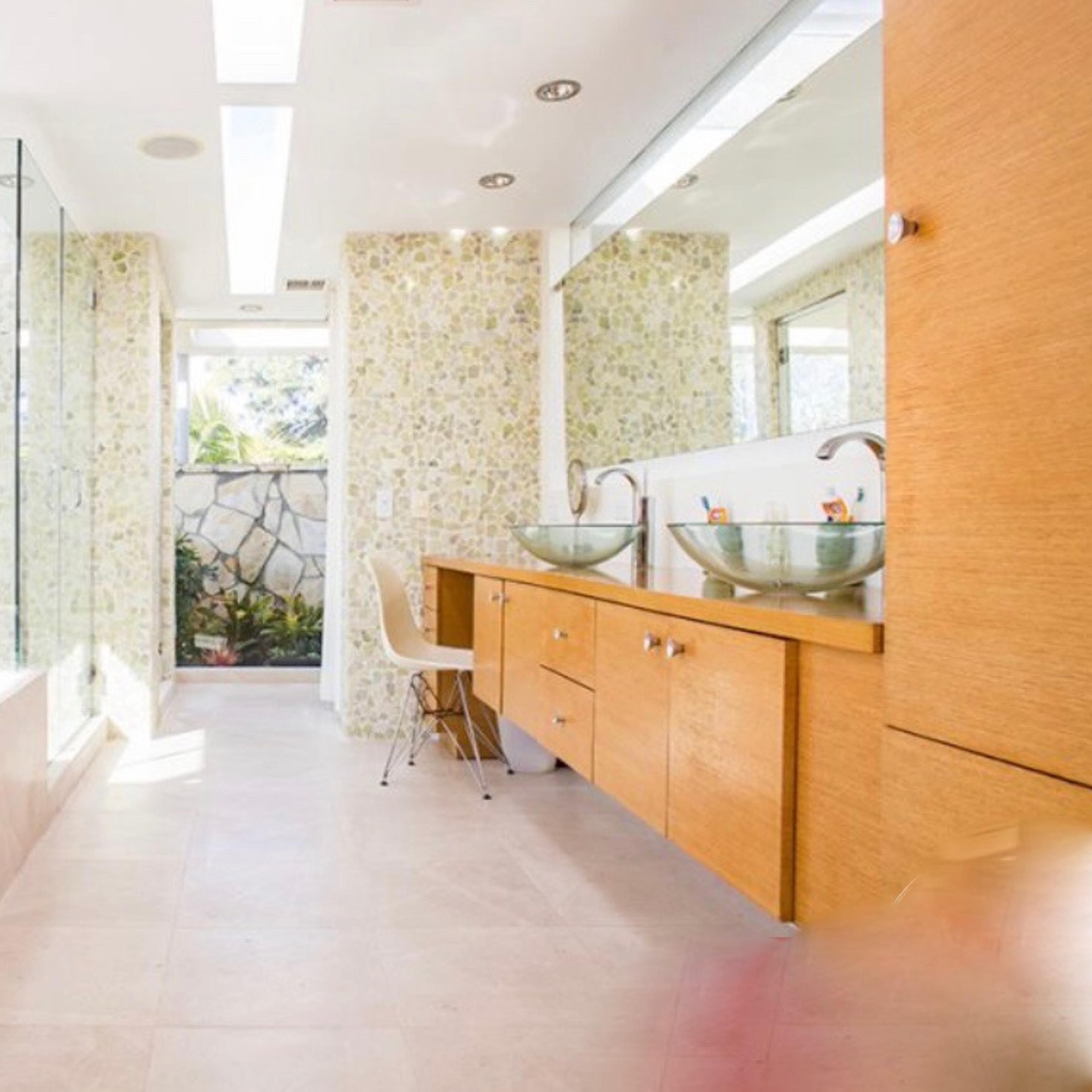 A modern bathroom featuring a glass shower, a freestanding bathtub, dual sinks with bowl-style basins, and large windows allowing natural light.