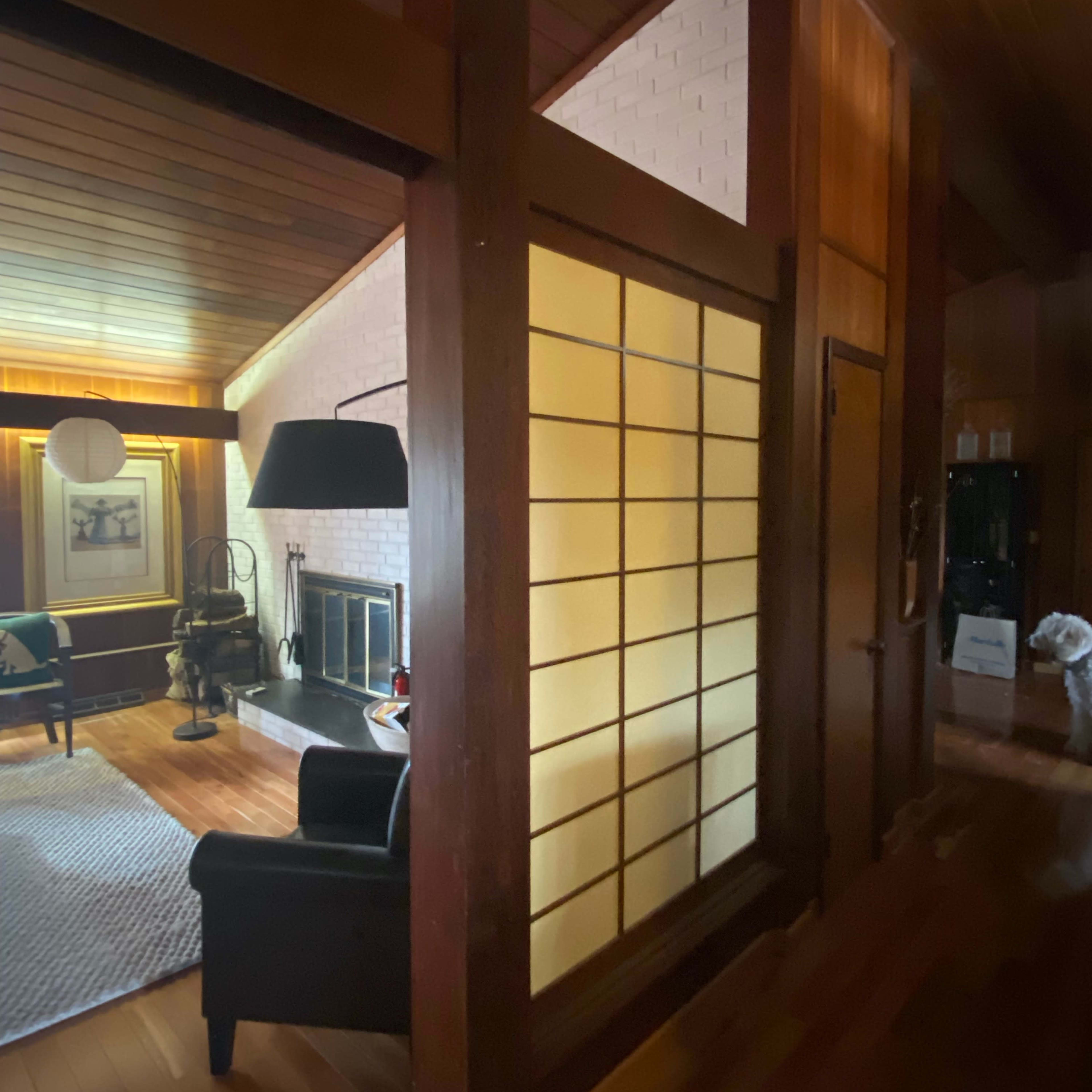 A wooden interior with a view of a room featuring a fireplace, a black armchair, and a partition with shoji-style sliding doors.