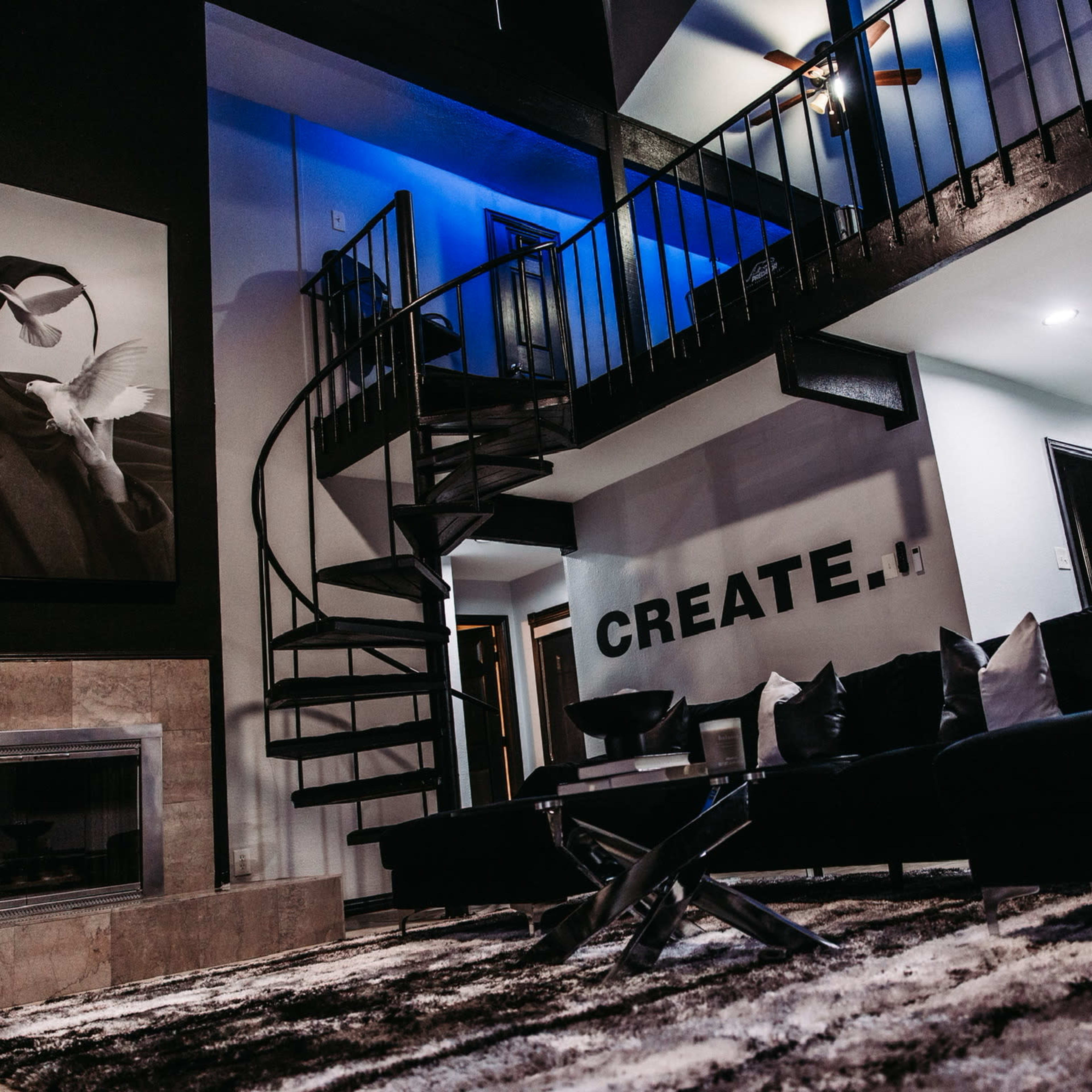 A modern interior featuring a spiral staircase, a large black-and-white artwork on the wall, and a living area with dark furniture and a patterned backdrop.