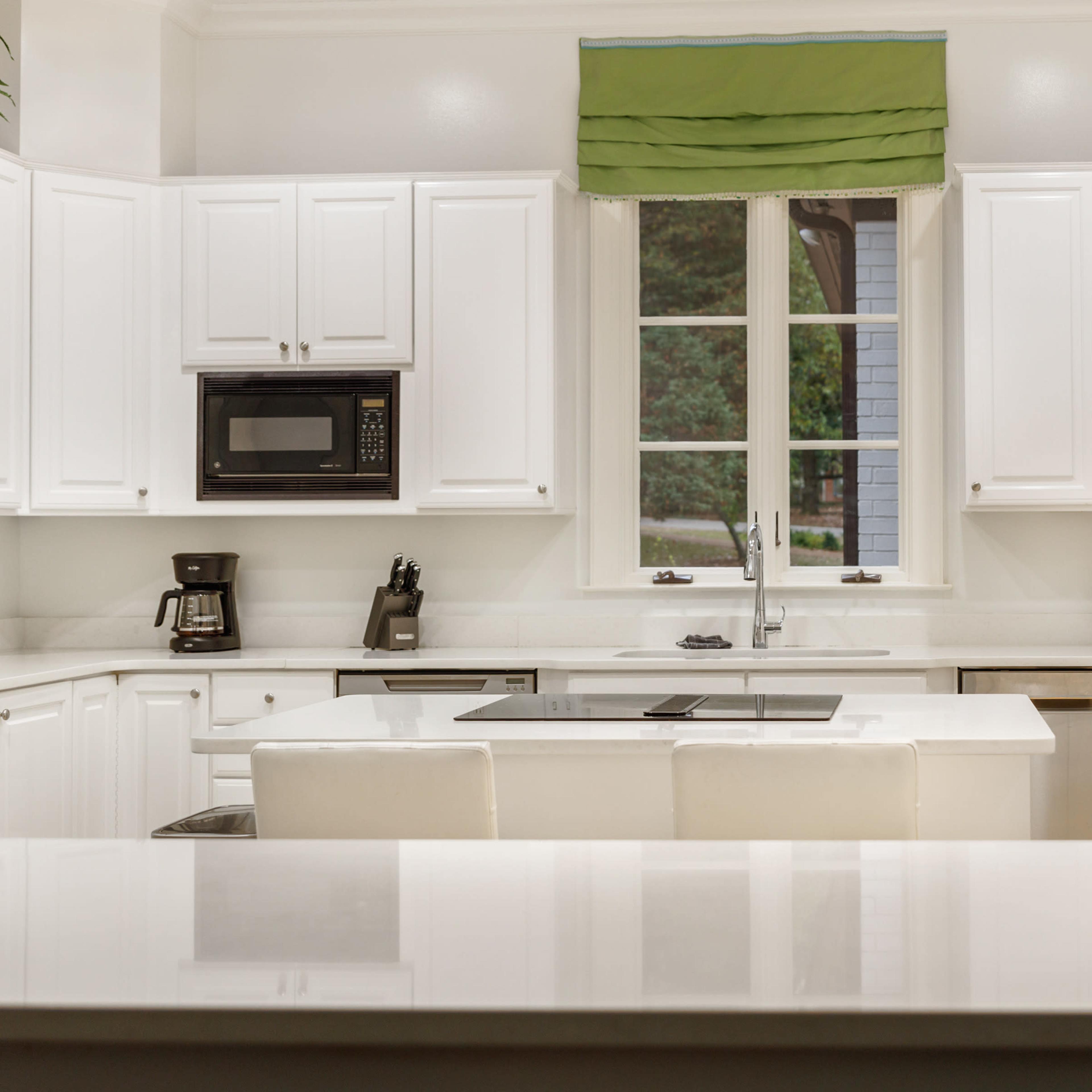 A bright kitchen with white cabinetry, a central island with seating, and appliances including a microwave and coffee maker.