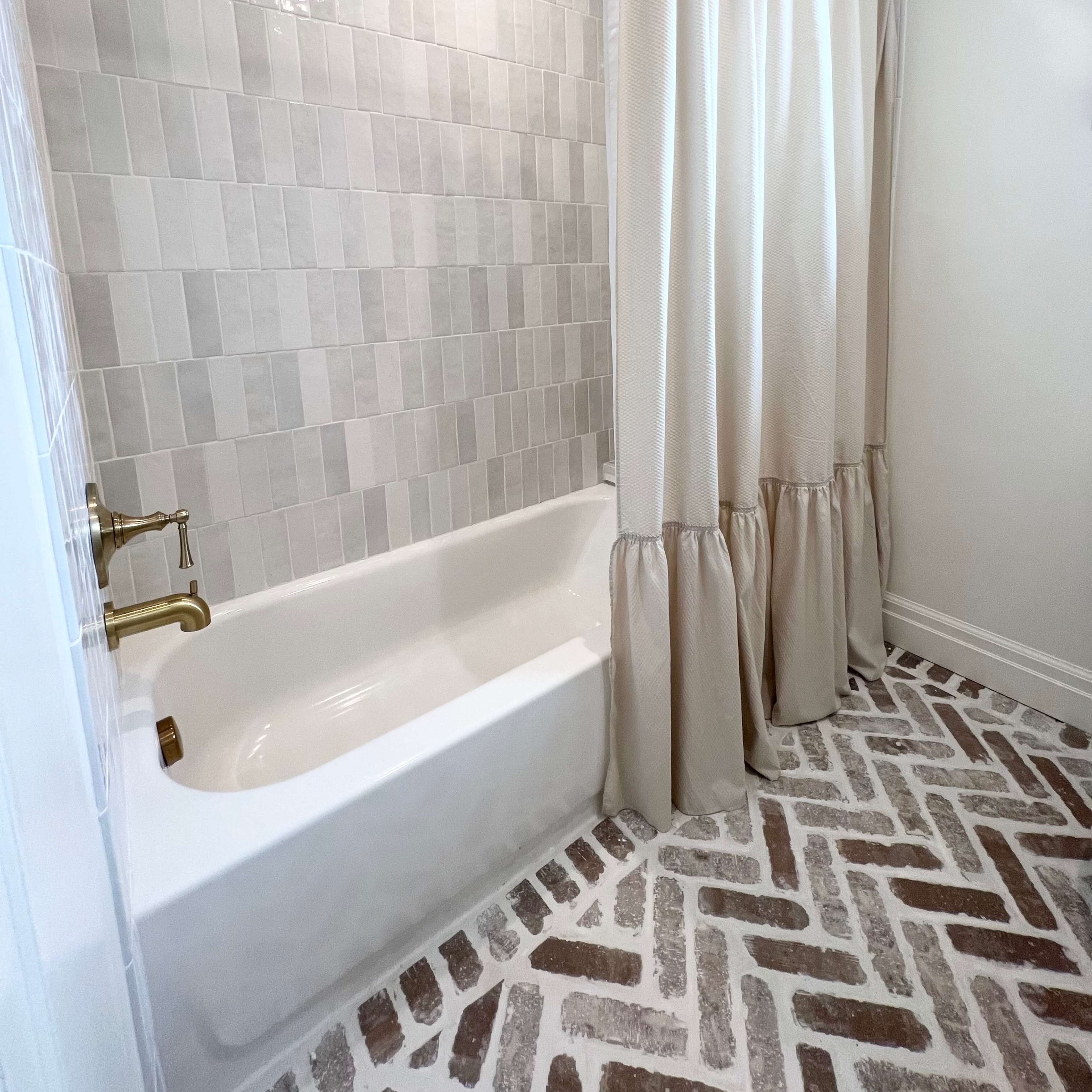 A bathroom featuring a tub with a shower curtain, a tiled wall, and a patterned floor.