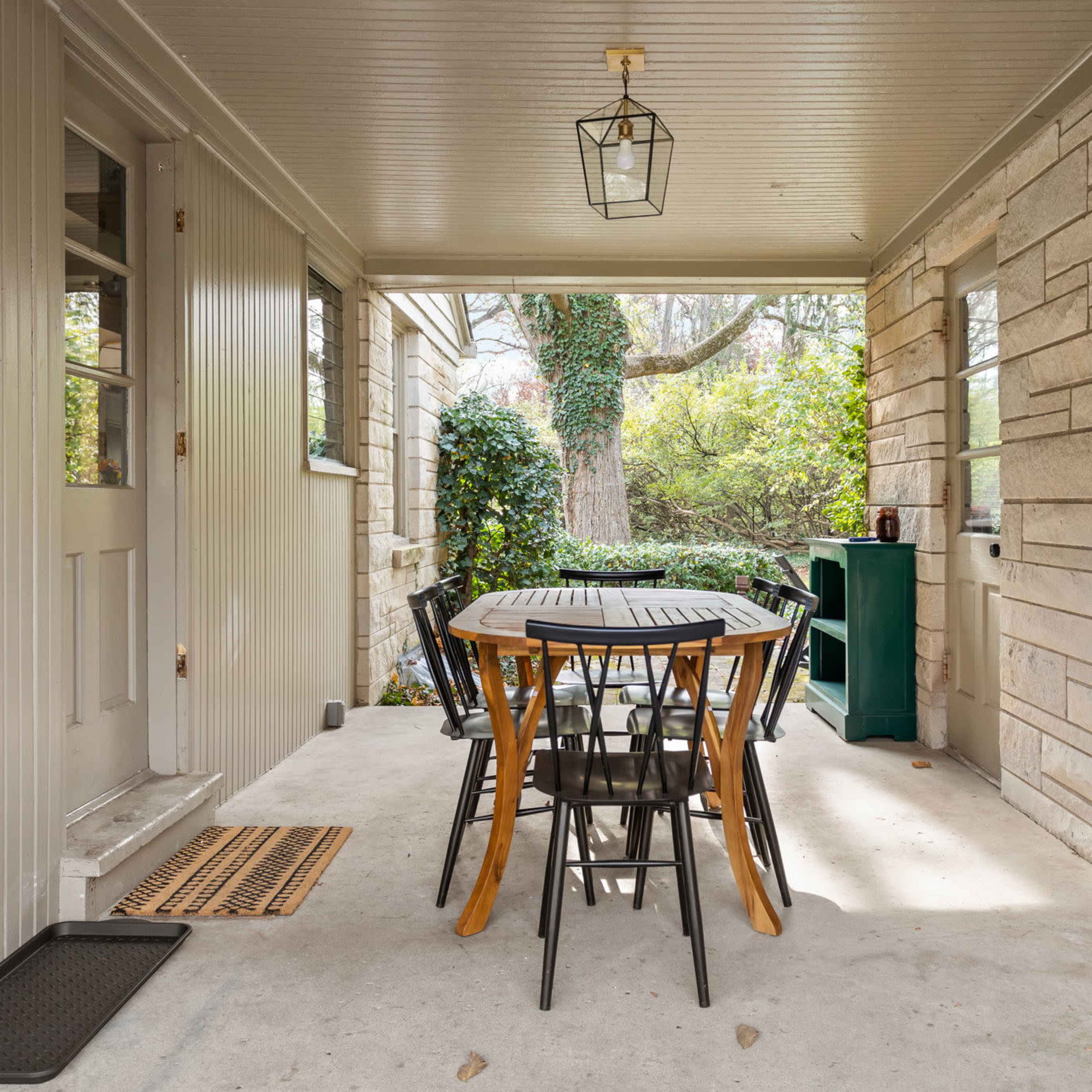 A covered outdoor patio featuring a round table with four chairs, a small green cabinet, and a lantern hanging from the ceiling.