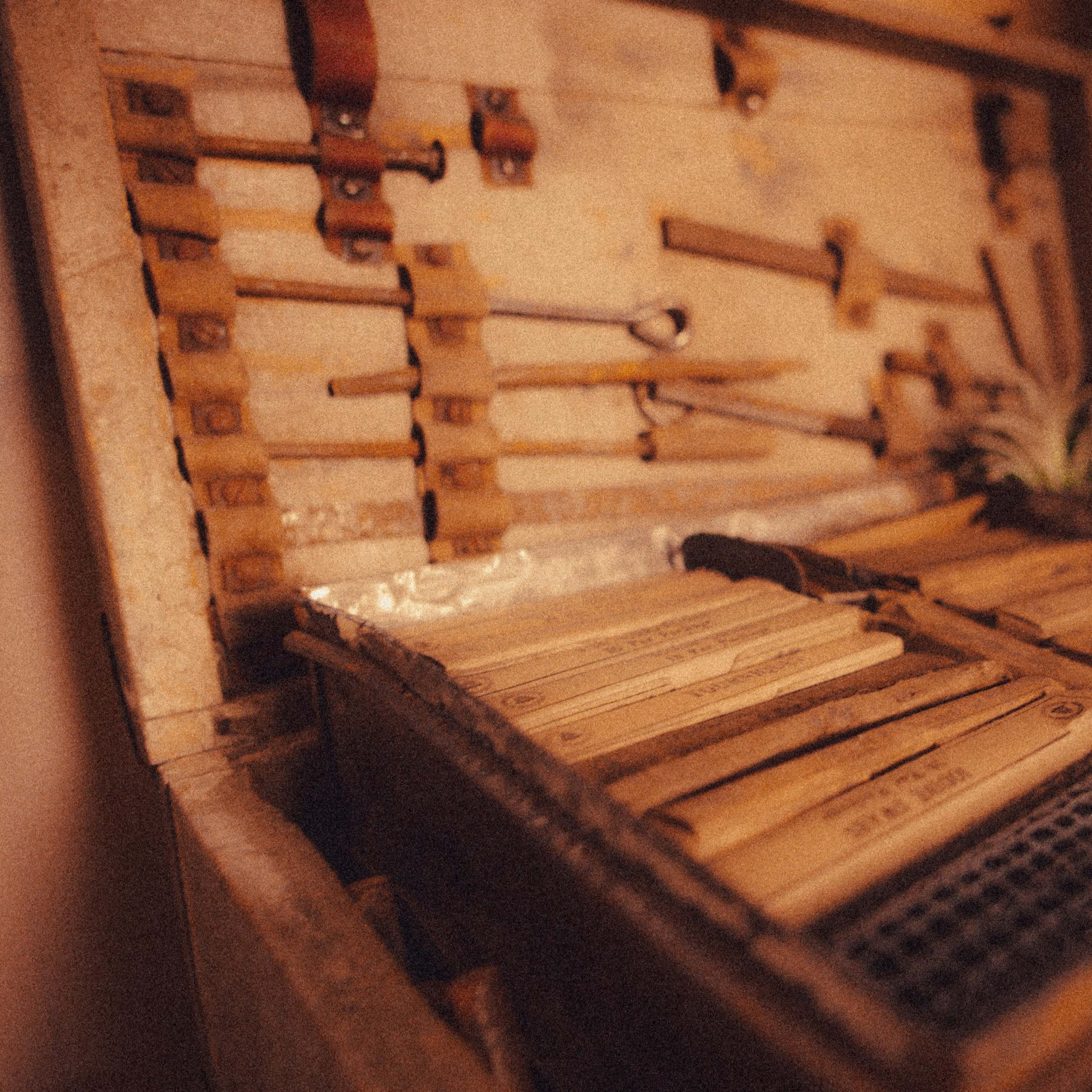 A wooden toolbox is filled with various tools and neatly organized wooden sticks, surrounded by plants.